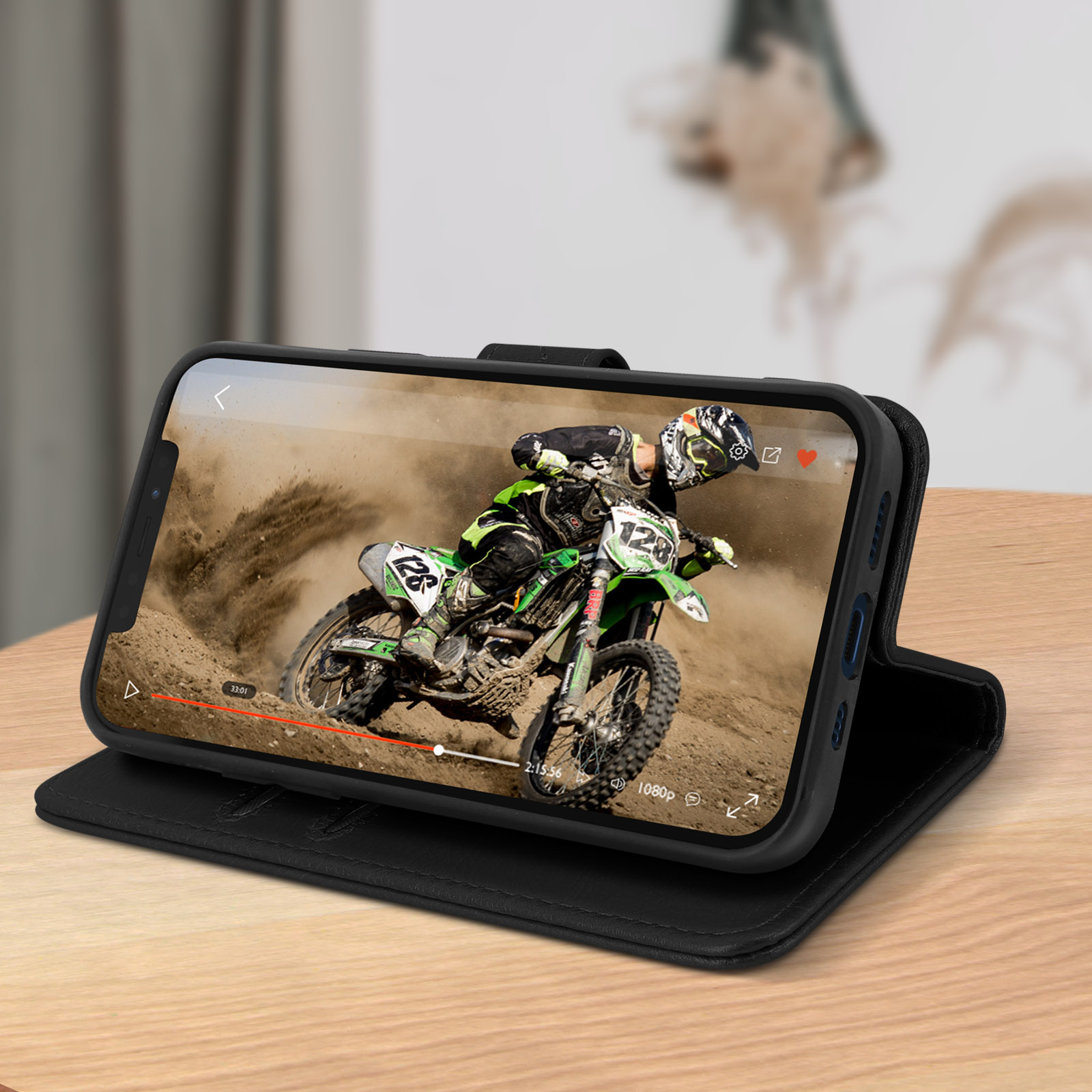 Een telefoon in een zwarte hoes met een motocrossvideo, op een houten tafel.