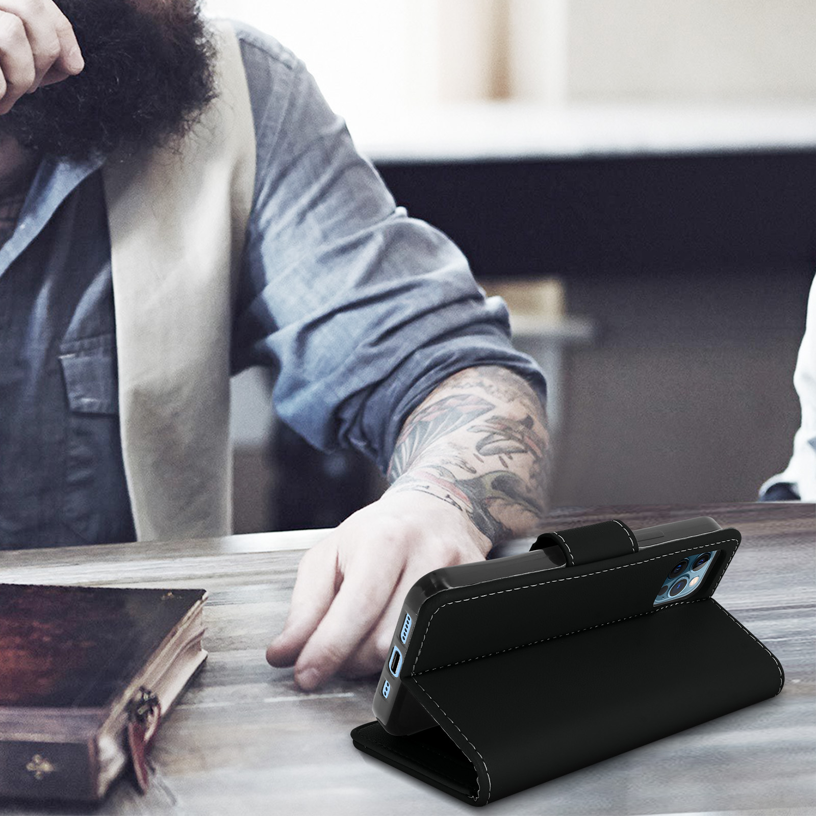 Een zwarte telefoonhoes ligt open op een tafel. Een man met een baard staat op de achtergrond.