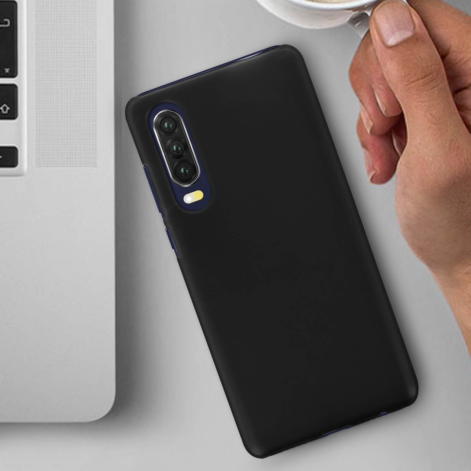 Una custodia nera per telefono su una superficie, con un laptop sullo sfondo e una tazza.