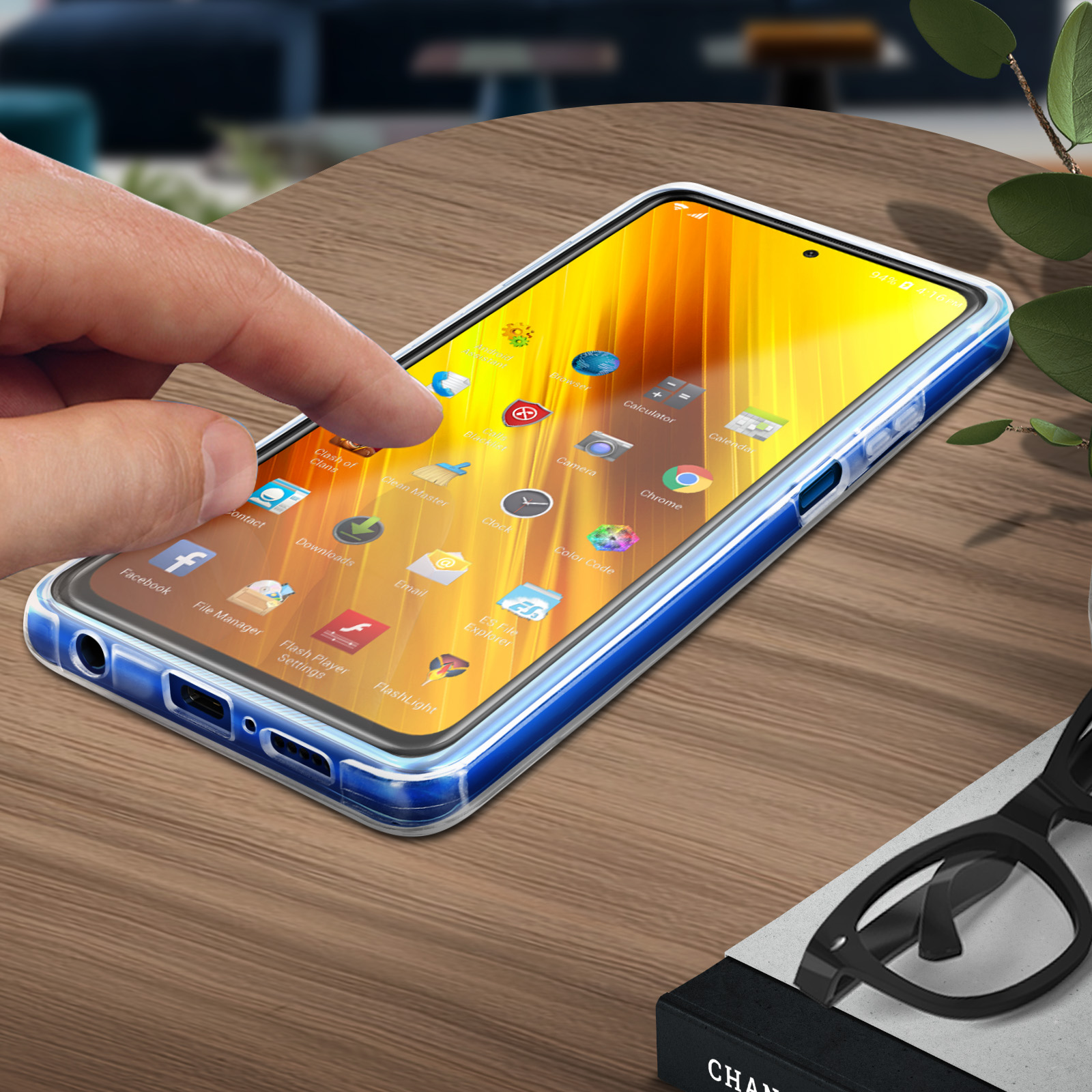 Une main touche l'écran d'un téléphone. Le téléphone a une coque bleue et est sur une table en bois.