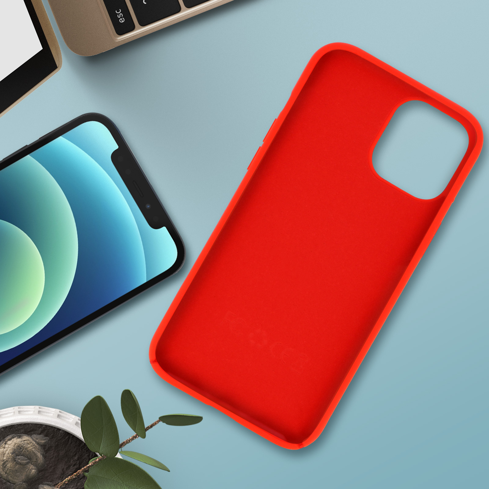 Rode telefoonhoes en een telefoon, beide op een blauw oppervlak met een kleine plant en een toetsenbord.