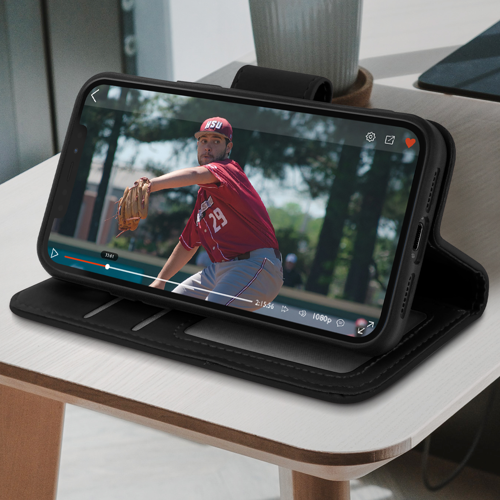 Telefono in custodia nera su un tavolo, riproduce un video di un lanciatore di baseball sullo schermo.