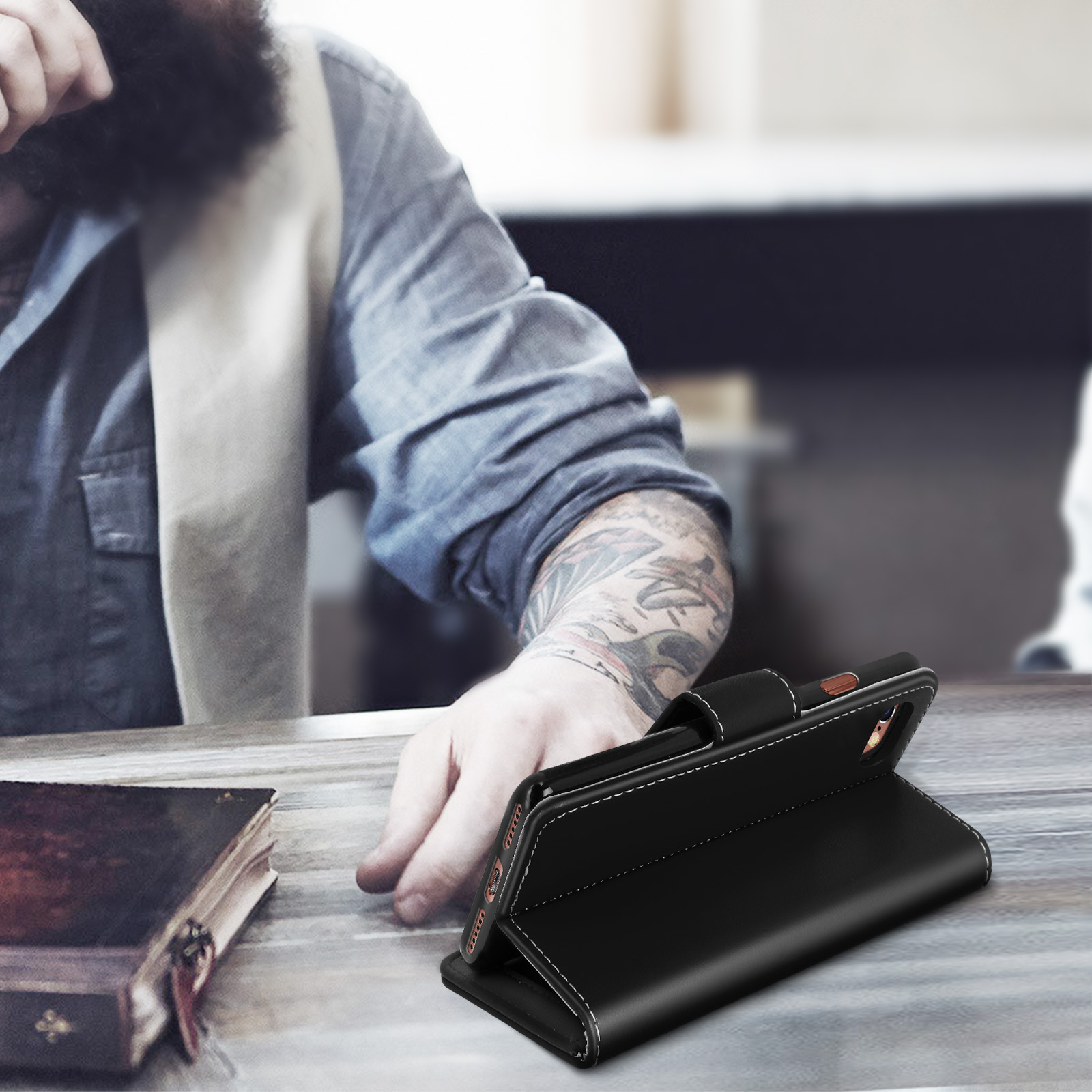 Un uomo seduto a un tavolo con un libro e una custodia nera per telefono sollevata.