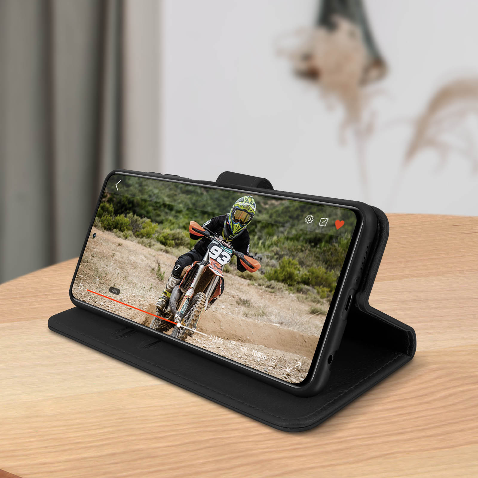 Un téléphone dans un étui noir montrant une vidéo d'une course de moto-cross. Le téléphone est sur une table.
