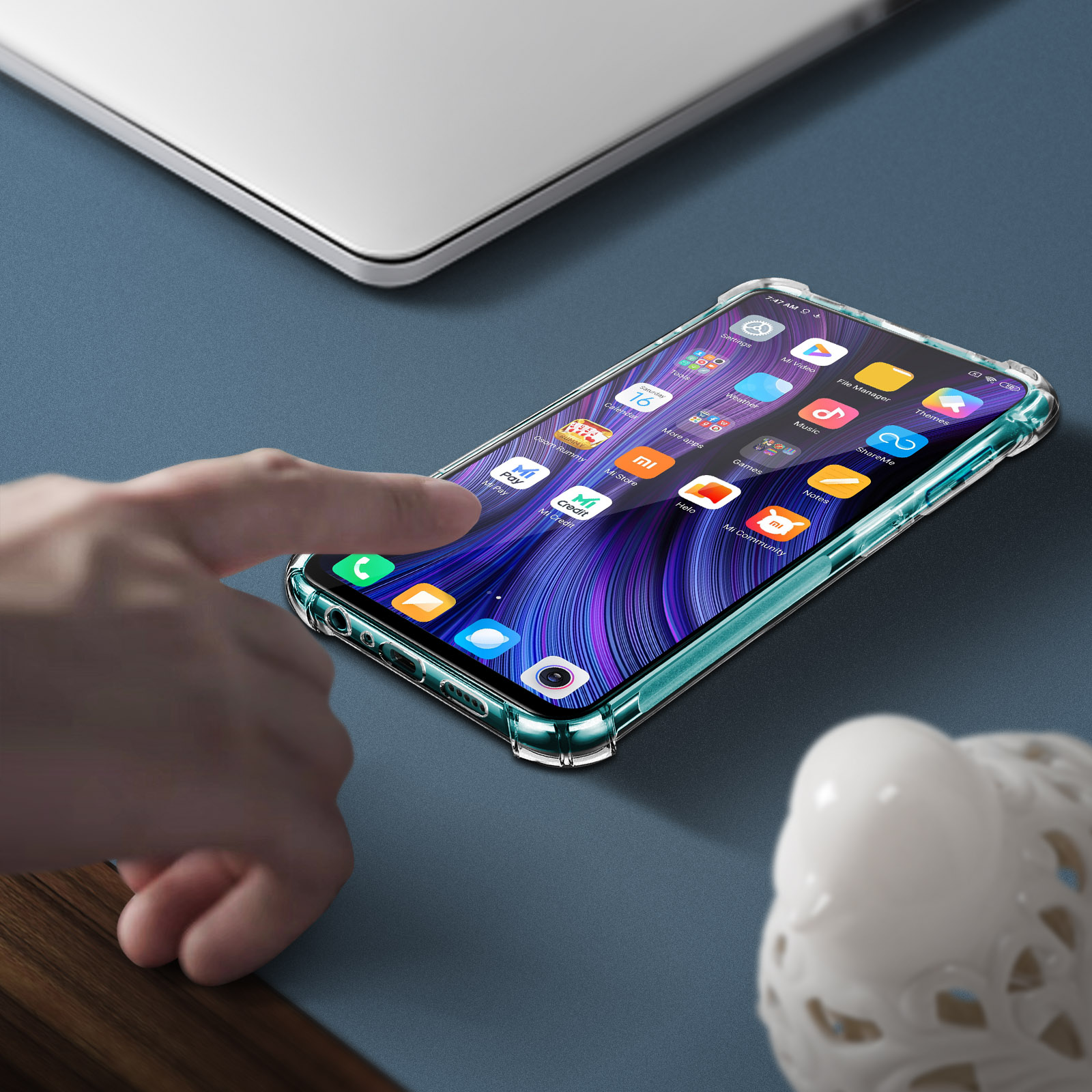 Una mano tocca lo schermo di un telefono. Il telefono è in una custodia trasparente. Nelle vicinanze c'è una statuina bianca.