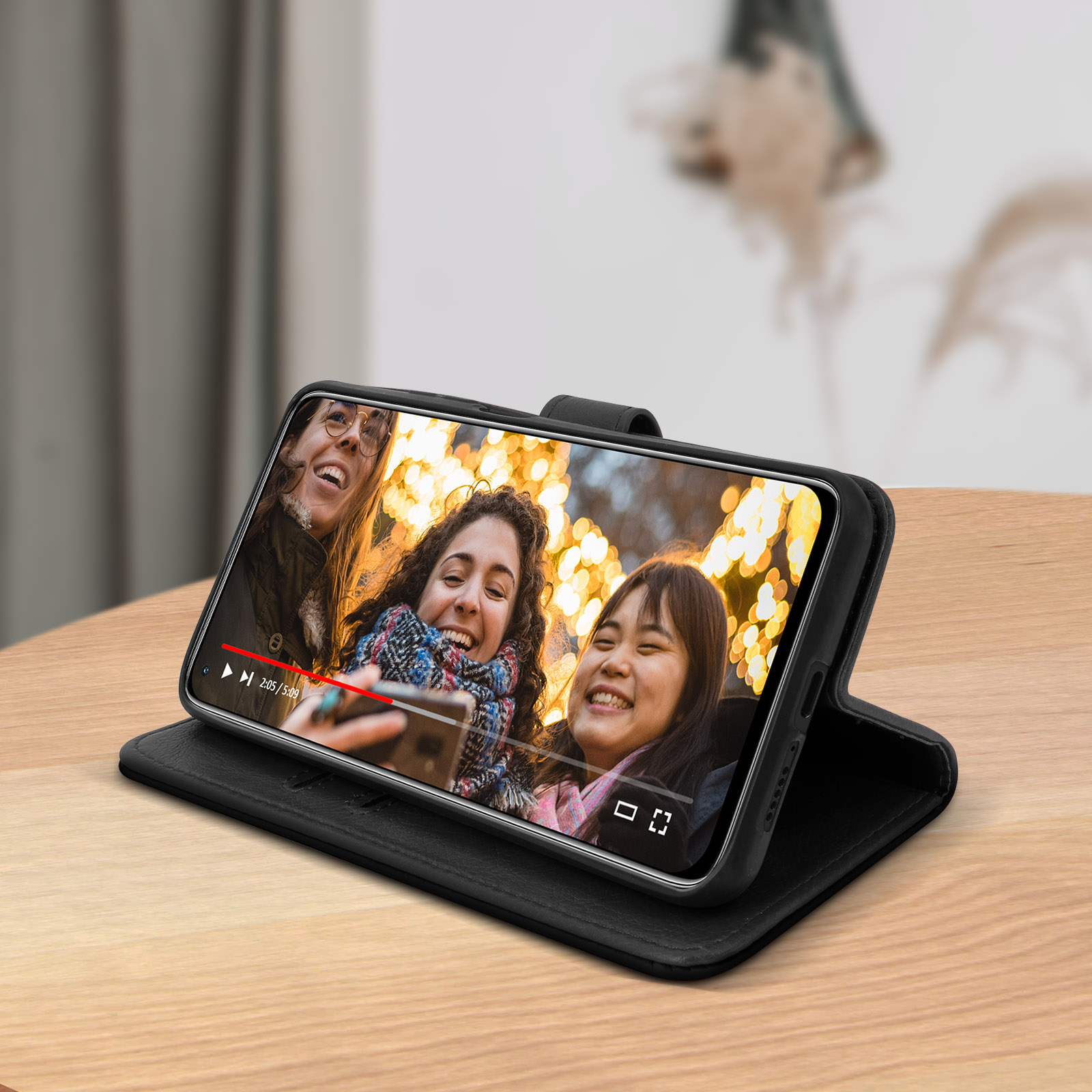 Un telefono mostra un video di persone. Il telefono è in una custodia nera, appoggiato su una superficie di legno.