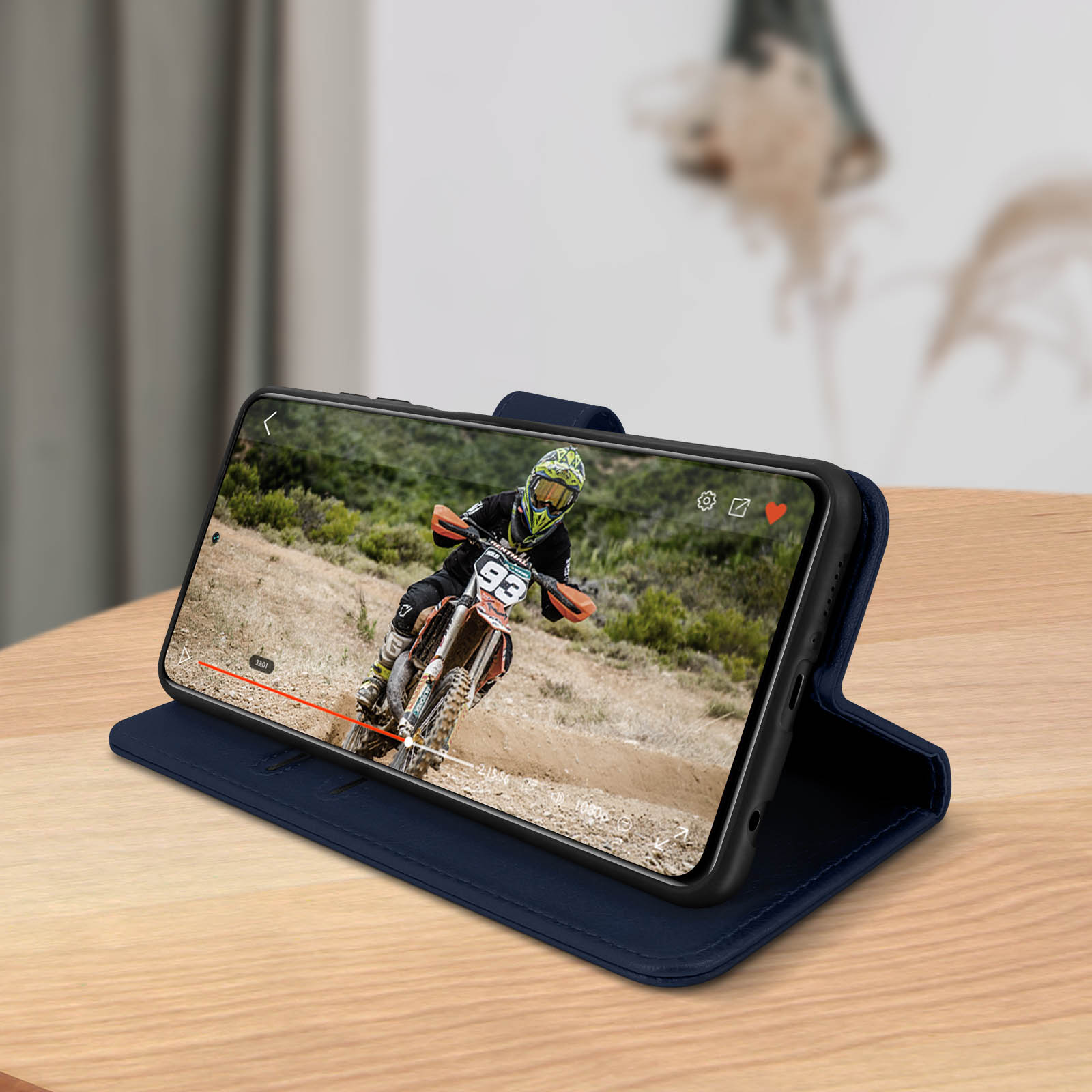 Telefono nella custodia che mostra il video di una gara motociclistica. Sfondo: tavolo in legno, stanza sfocata.
