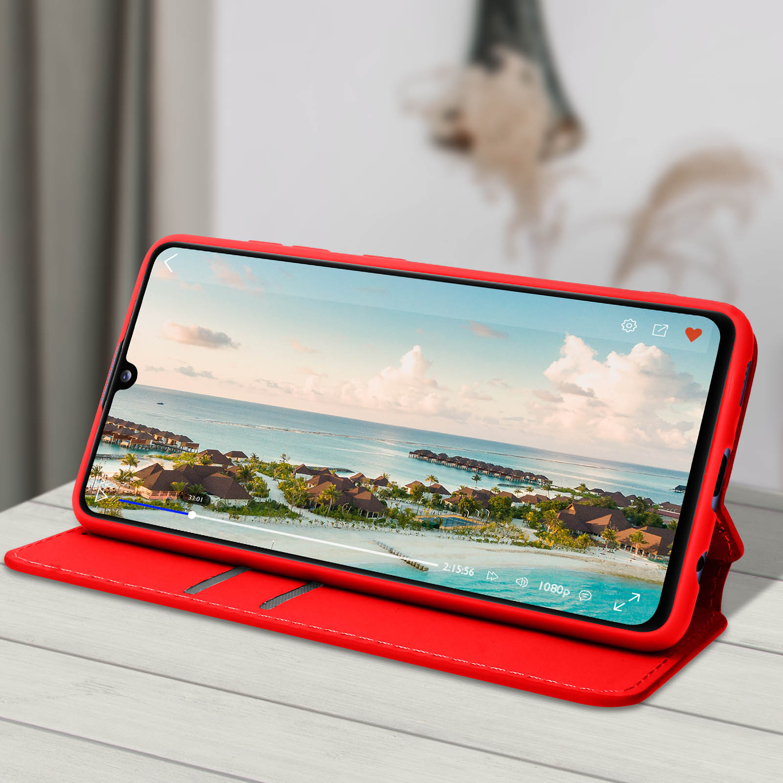 Telefon in roter Hülle, spielt Video mit Strand, Meer und blauem Himmel ab.