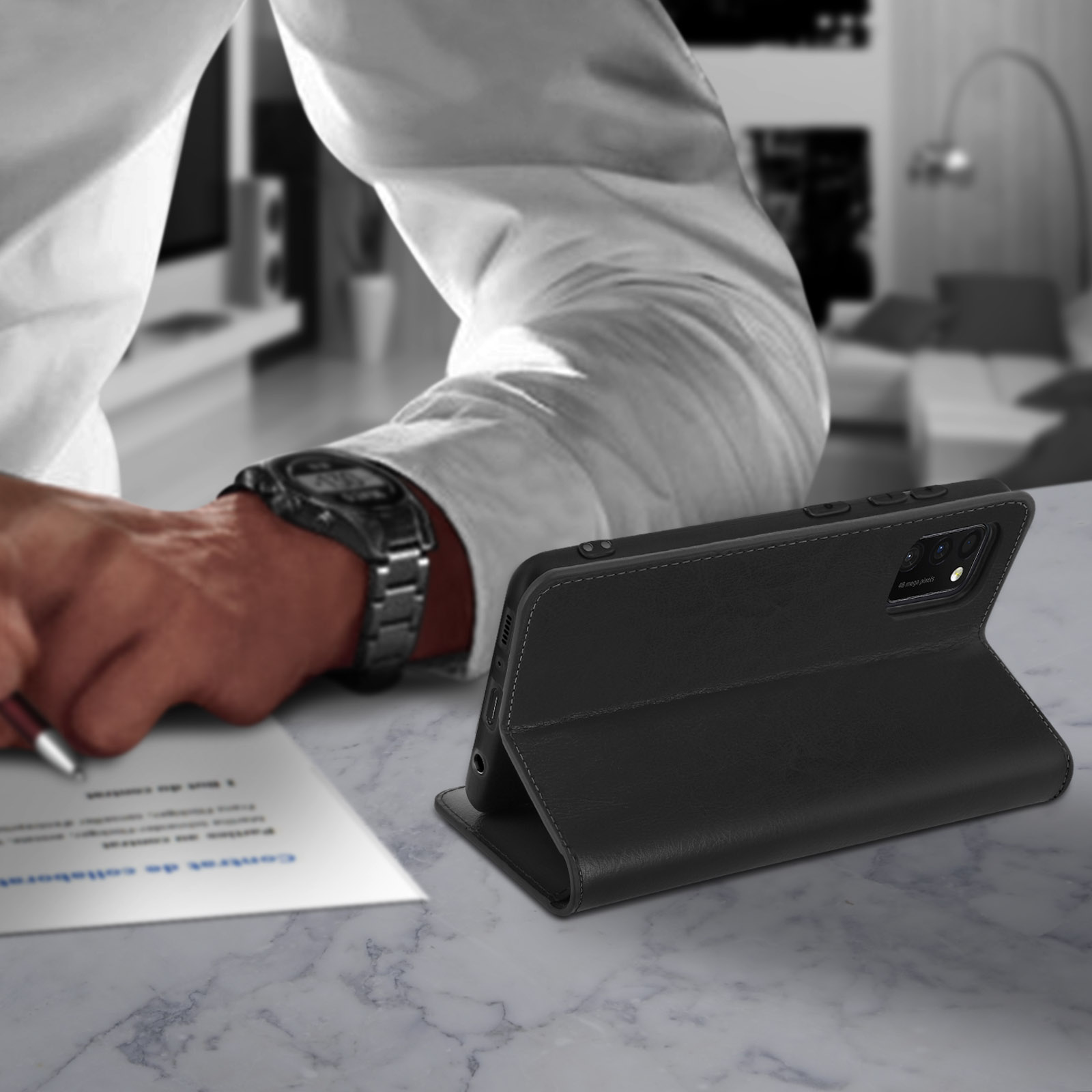 Zwarte telefoonhoes op marmeren tafel, persoon op de achtergrond die op een document schrijft.