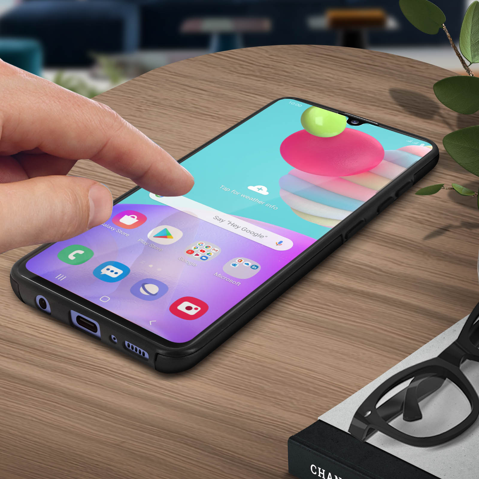 Main touchant un écran de téléphone noir avec des applications. Lunettes et boîte à proximité.