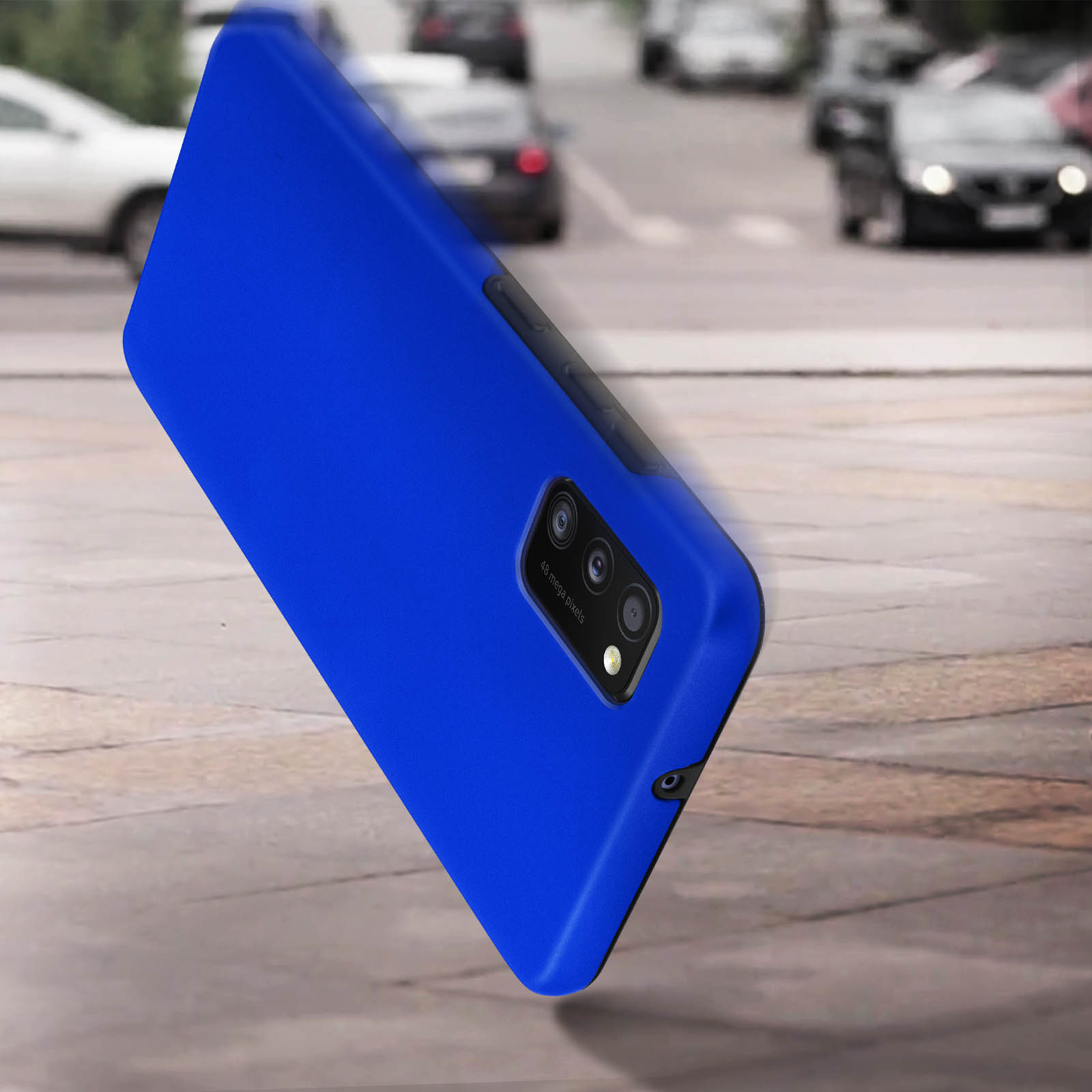 Una custodia blu per telefono sta cadendo. Auto guidano sullo sfondo sfocato, su una superficie grigia.