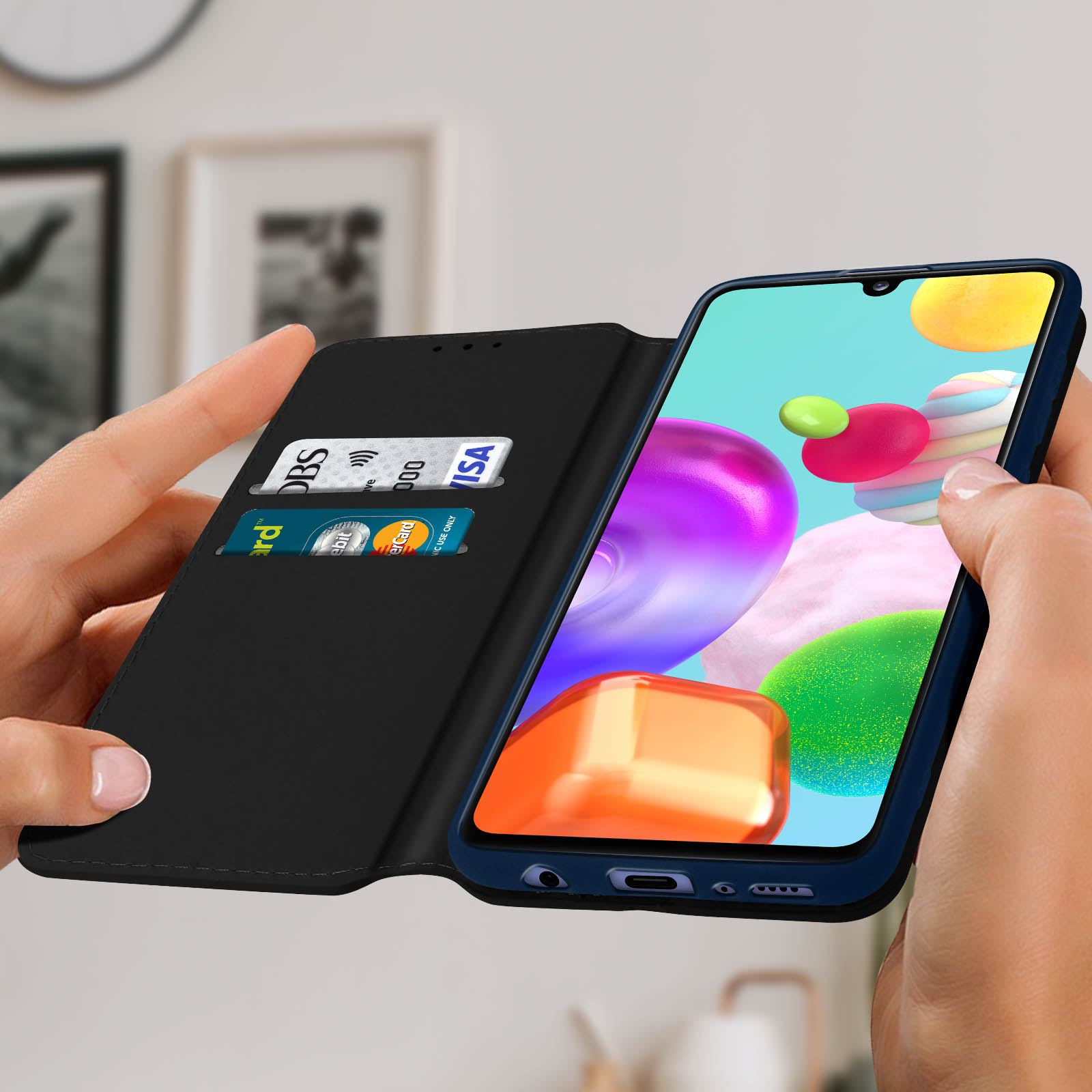 Hände halten eine Handyhülle, in der Kreditkarten sichtbar sind. Das Telefon zeigt ein farbenfrohes Display.