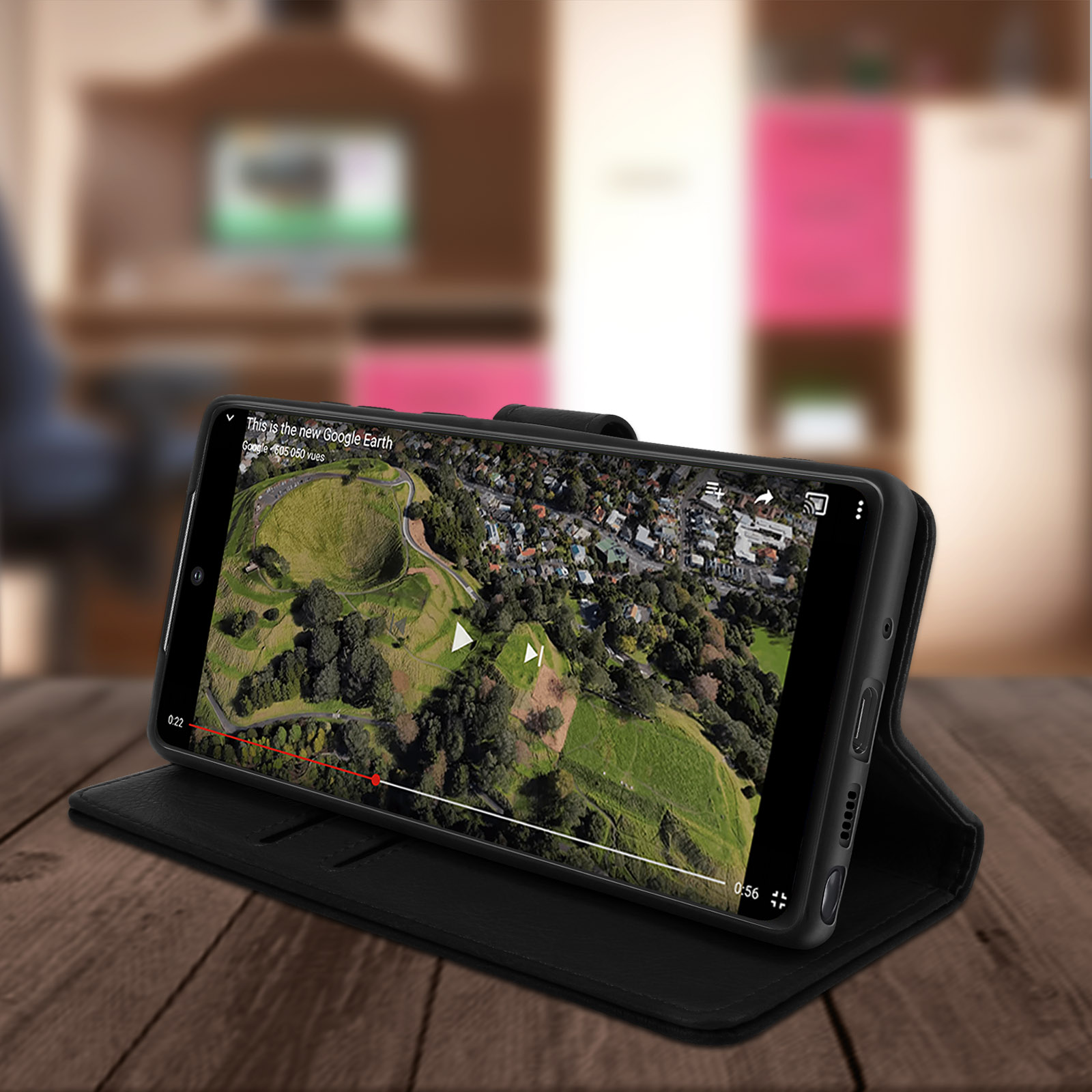 Un téléphone noir dans un étui, montrant une vidéo sur l'écran. L'étui est sur une table en bois.