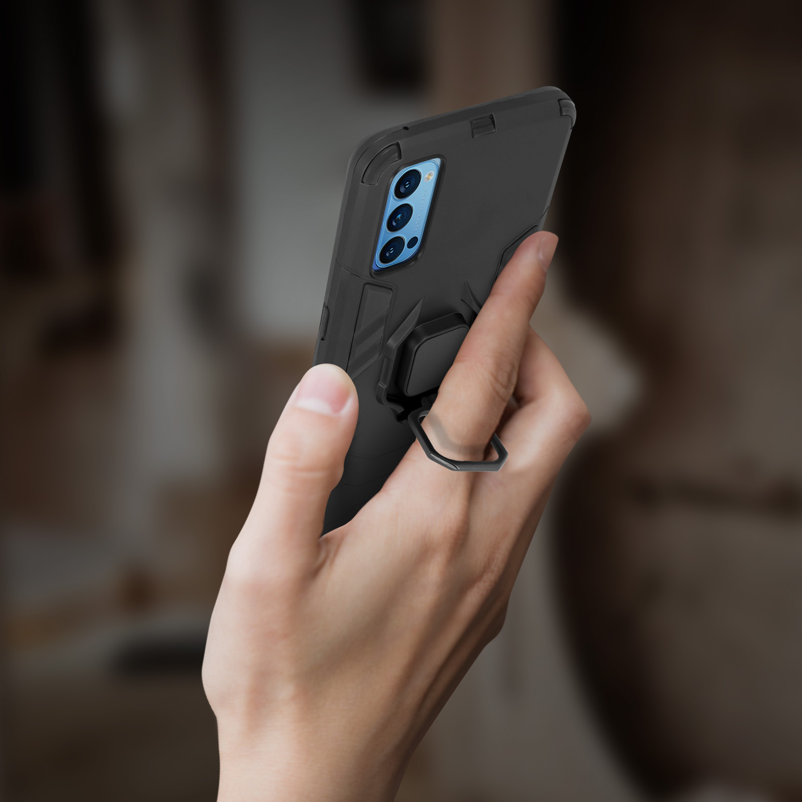 Une main tenant une coque de téléphone noire avec un support d'anneau, fond flou.