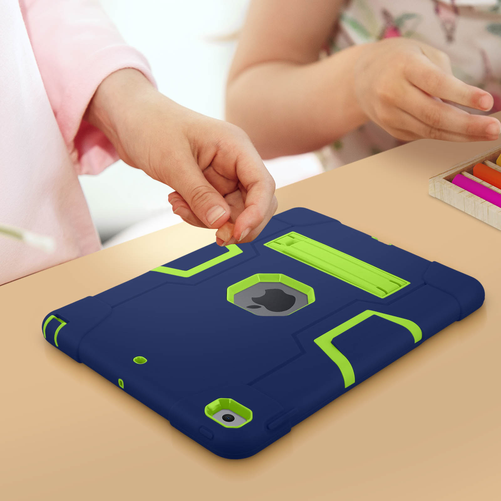 Blau-grüne iPad-Hülle, mit Kinderhand und Tisch.