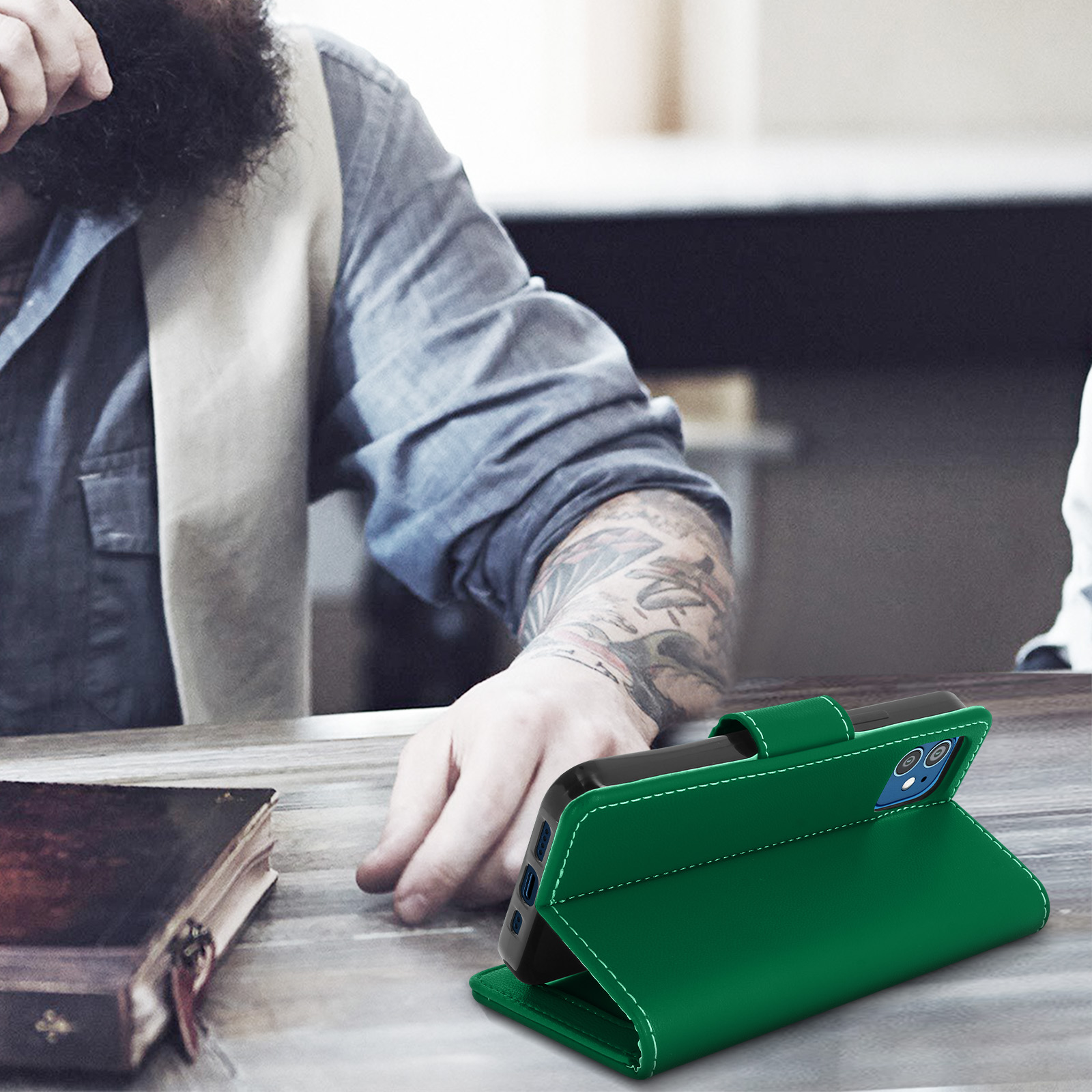 Groene telefoonhoes op een tafel. Persoon met tatoeages is zichtbaar op de achtergrond.