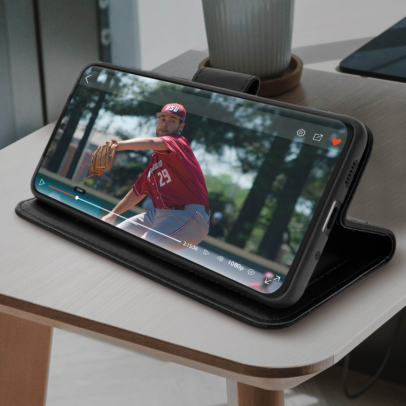 Telefono in custodia nera mostra partita di baseball. È appoggiato su un tavolo di legno.
