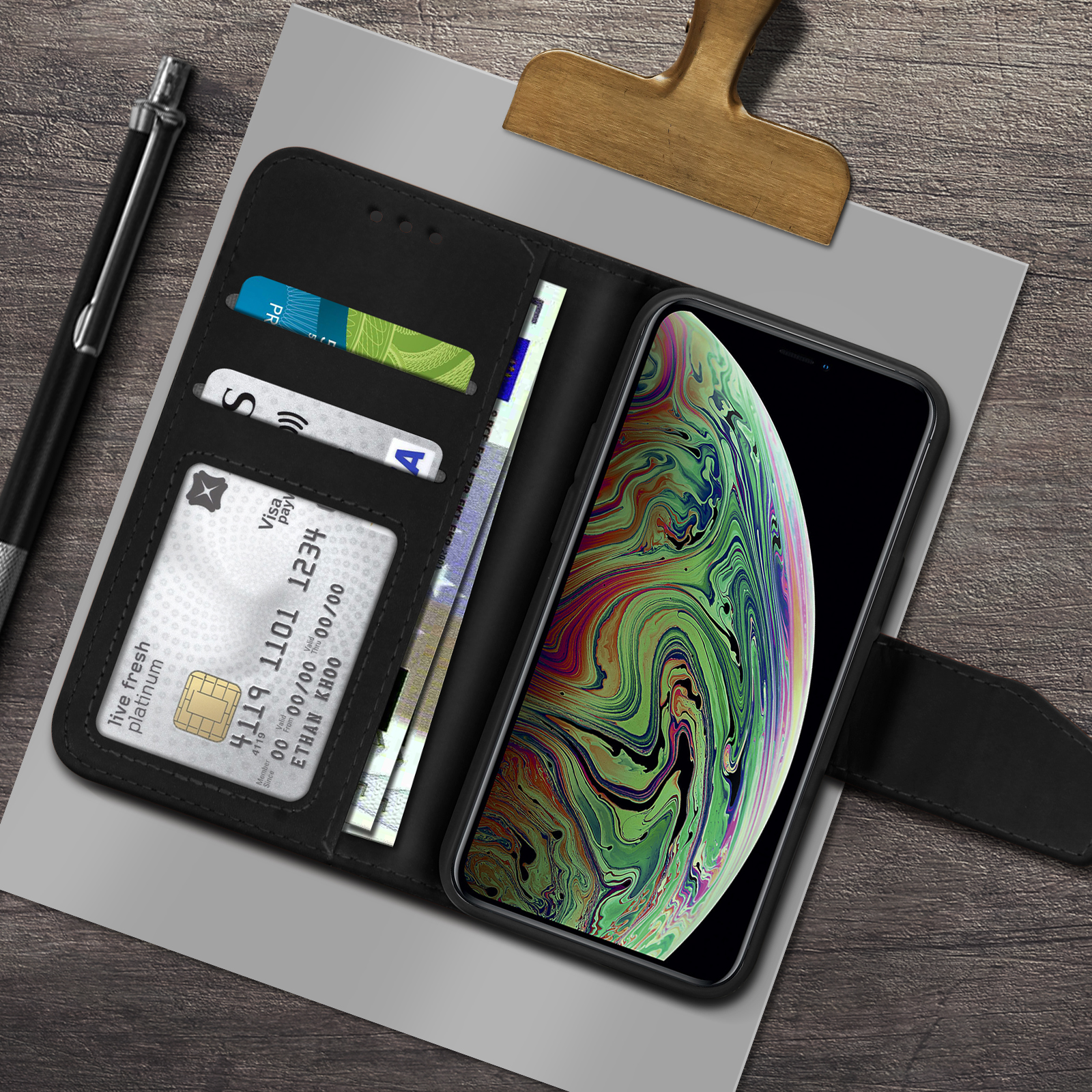 Een zwarte telefoon in een portefeuille met kaarten en geld. Een pen links op hout.