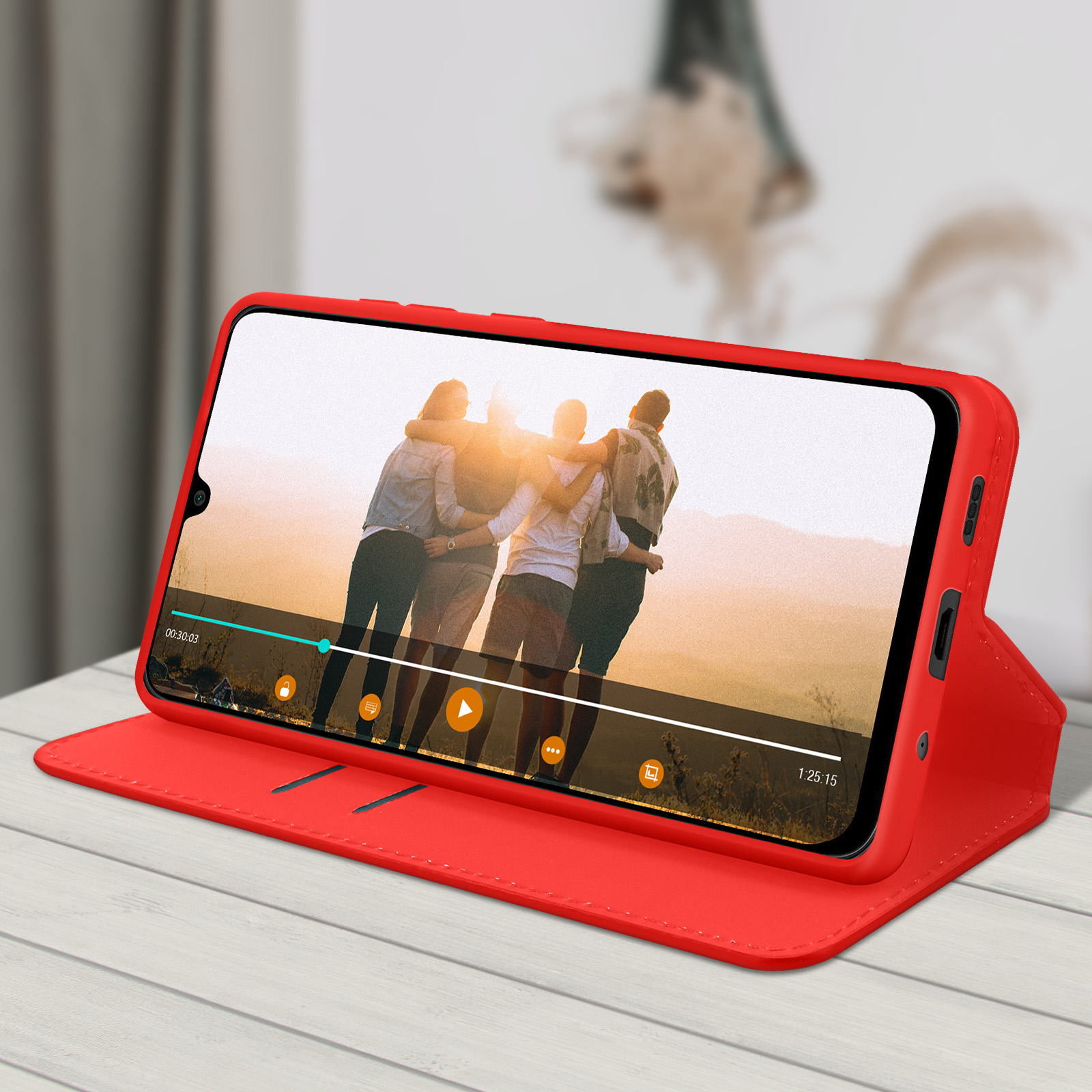 Custodia rossa per telefono con un telefono che mostra un video di persone, su un tavolo di legno.