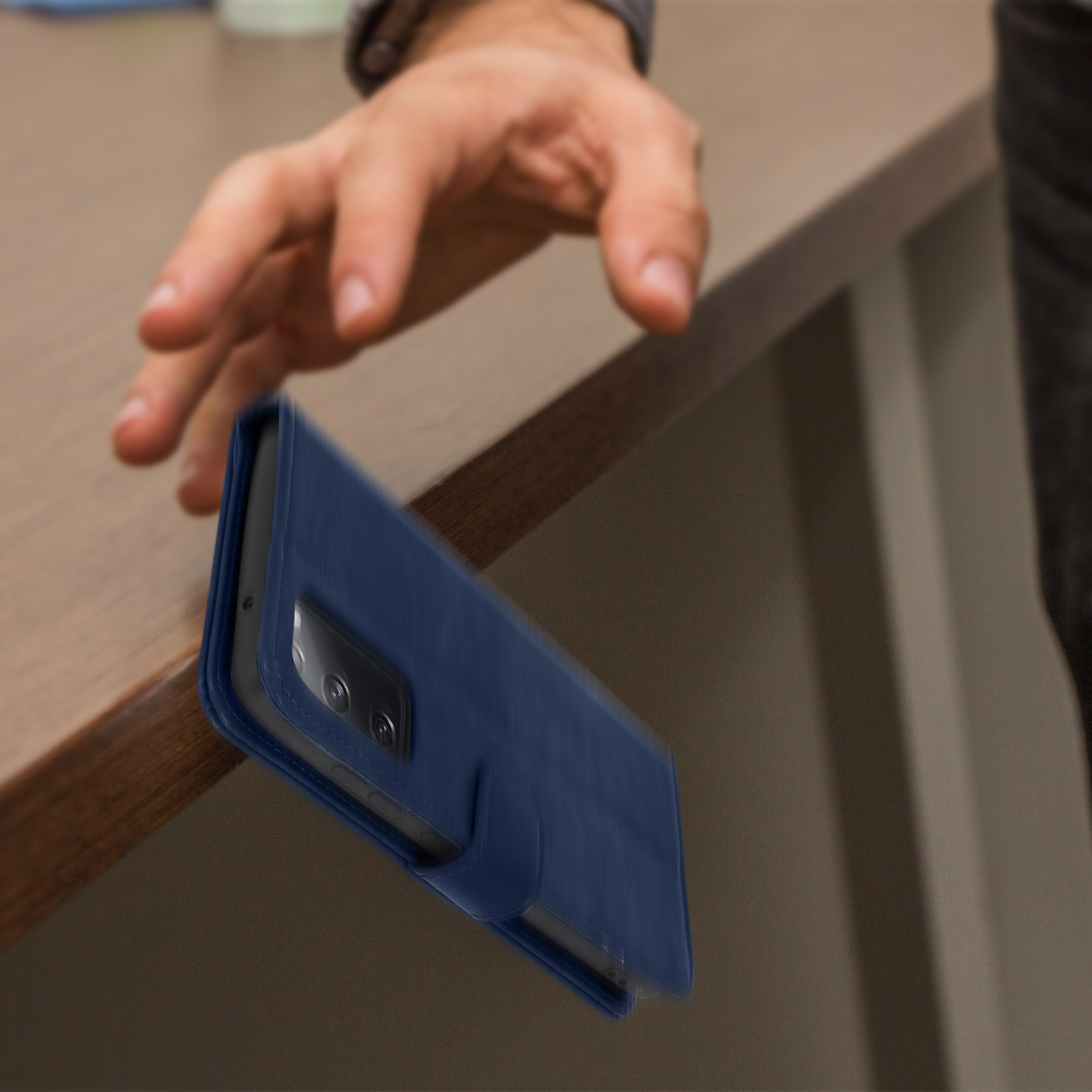 Hand die een blauwe telefoonhoes laat vallen, dicht bij een houten oppervlak.