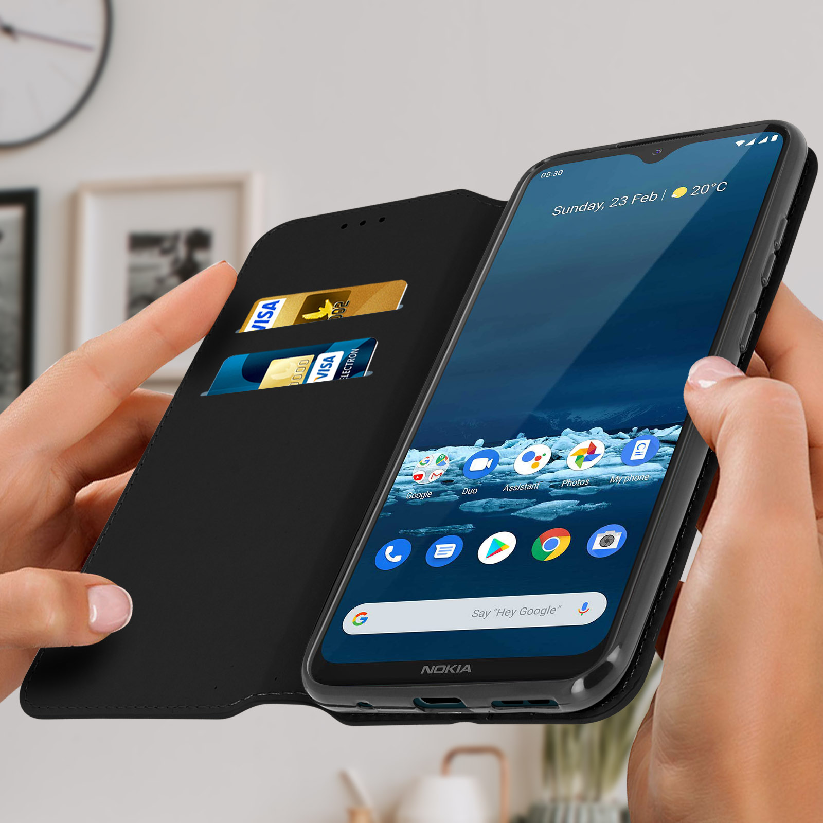 Een hand houdt een telefoon vast in een zwarte hoes met creditcards. Telefoonscherm zichtbaar. Vage achtergrond.
