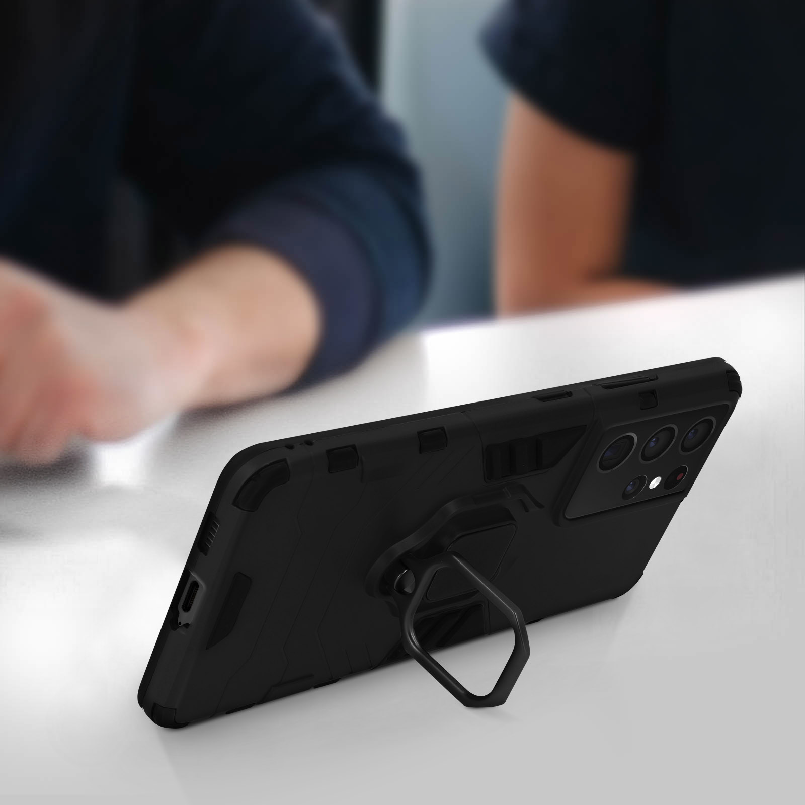 Custodia nera per telefono con supporto ad anello, con un telefono all'interno, su una superficie bianca.