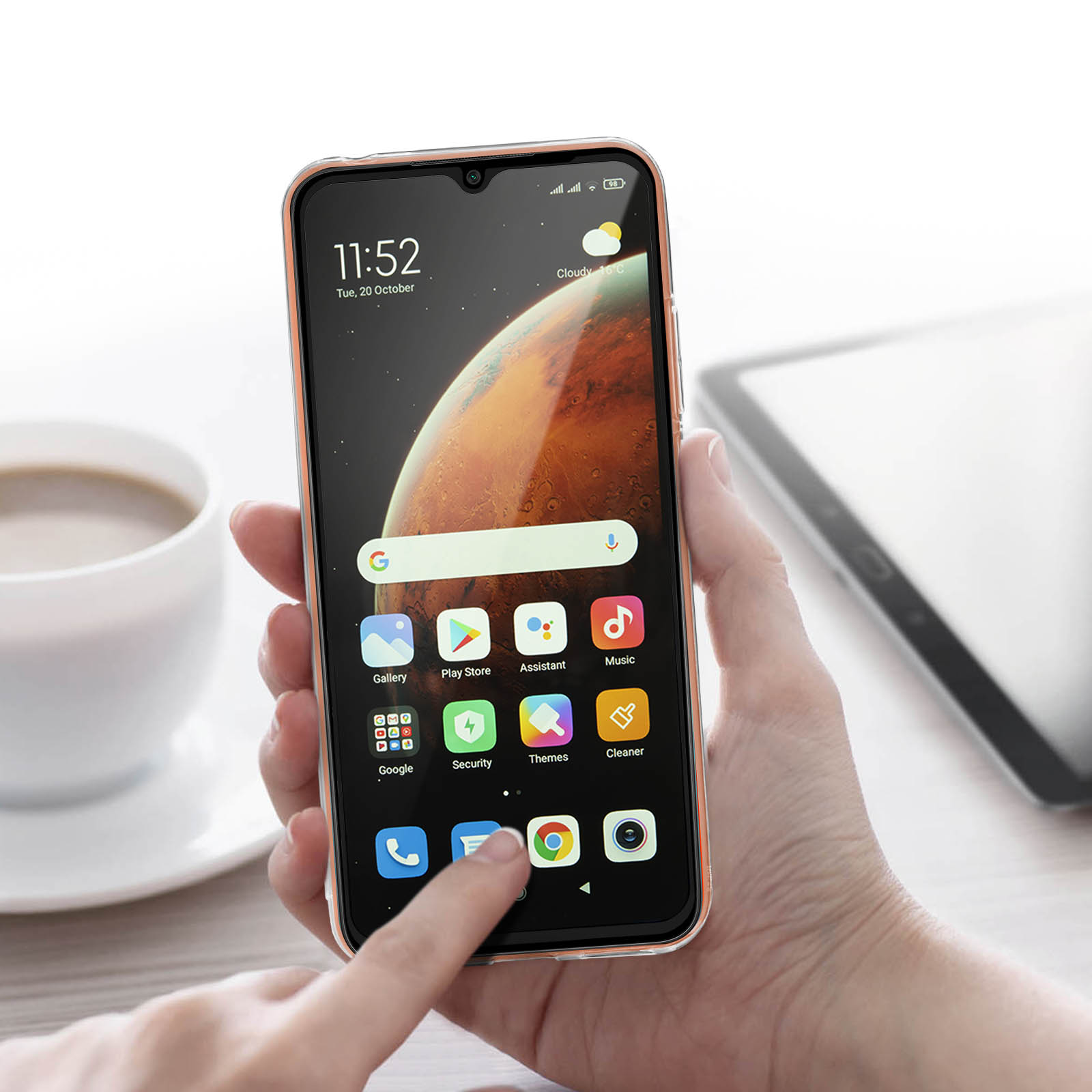 Una mano tiene un telefono che mostra uno schermo dell'app. Una tazza e un tablet sullo sfondo.