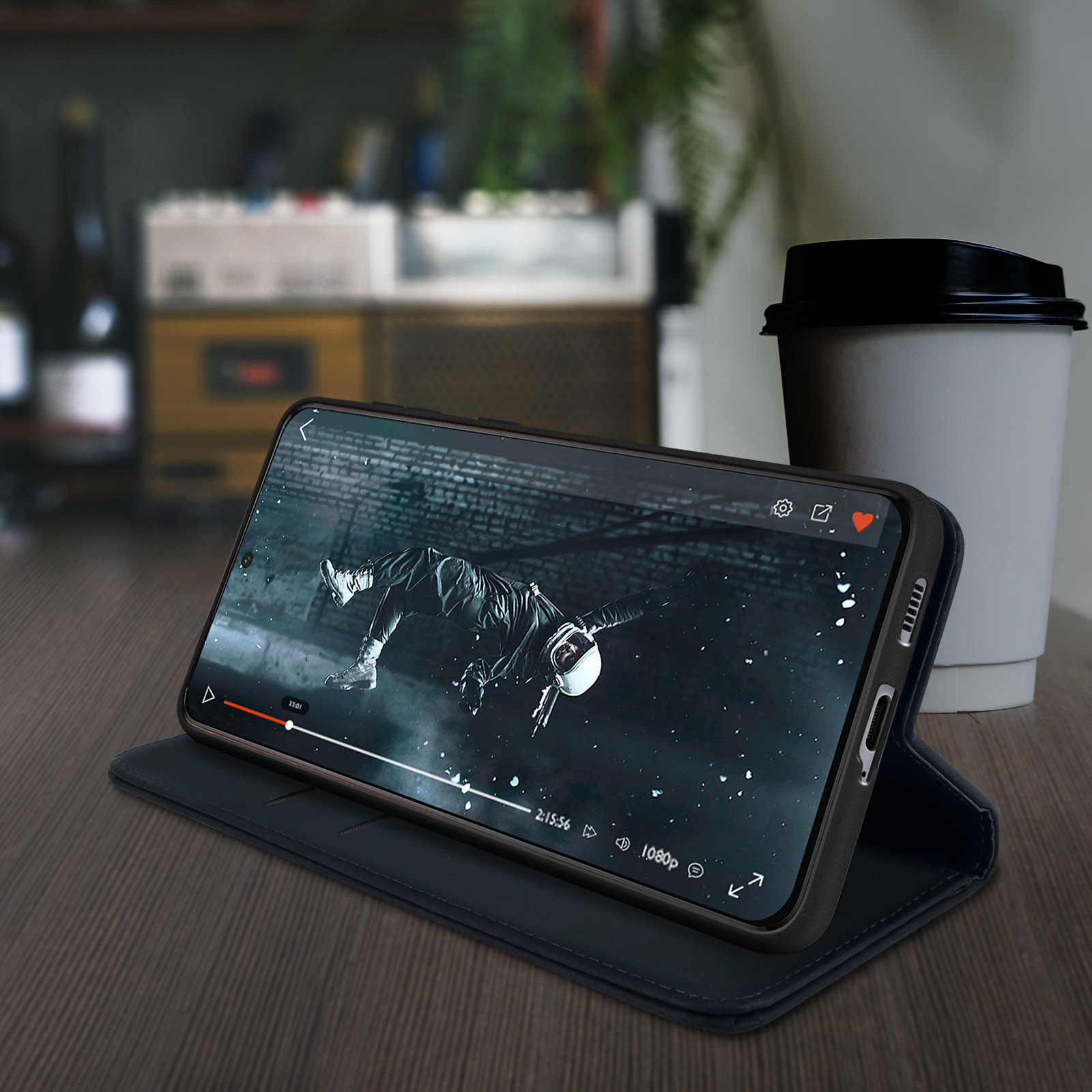 Un telefono che mostra un video, appoggiato su un tavolo con una tazza di caffè sullo sfondo. Sfondo scuro.