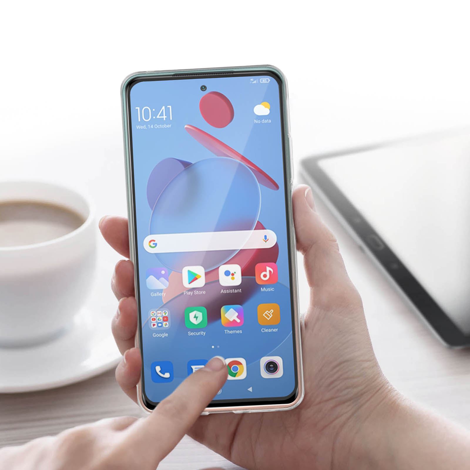 Una mano che tiene un telefono con icone di app sullo schermo, vicino a una tazza.