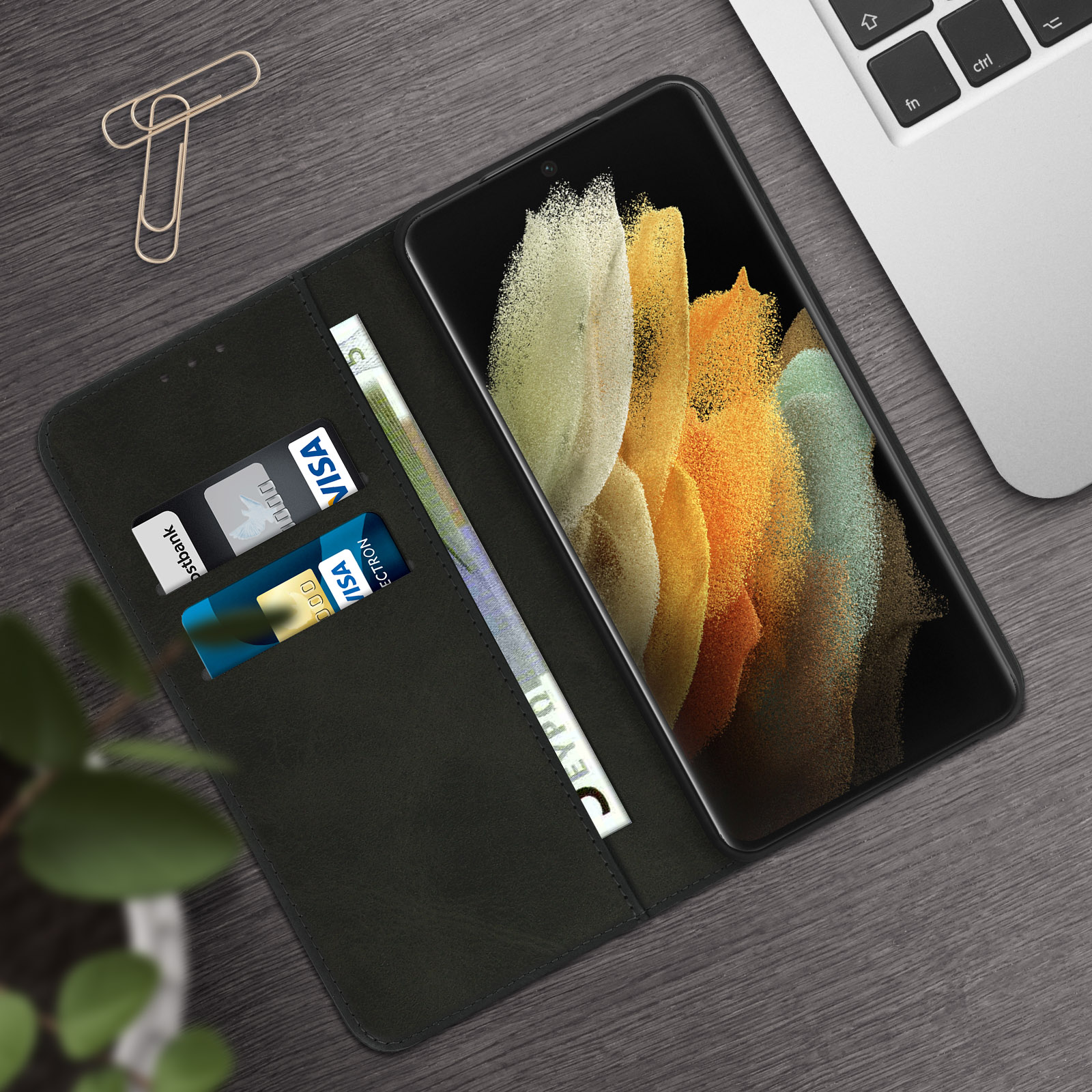 Custodia nera con telefono, carte di credito e banconote euro su un tavolo di legno.