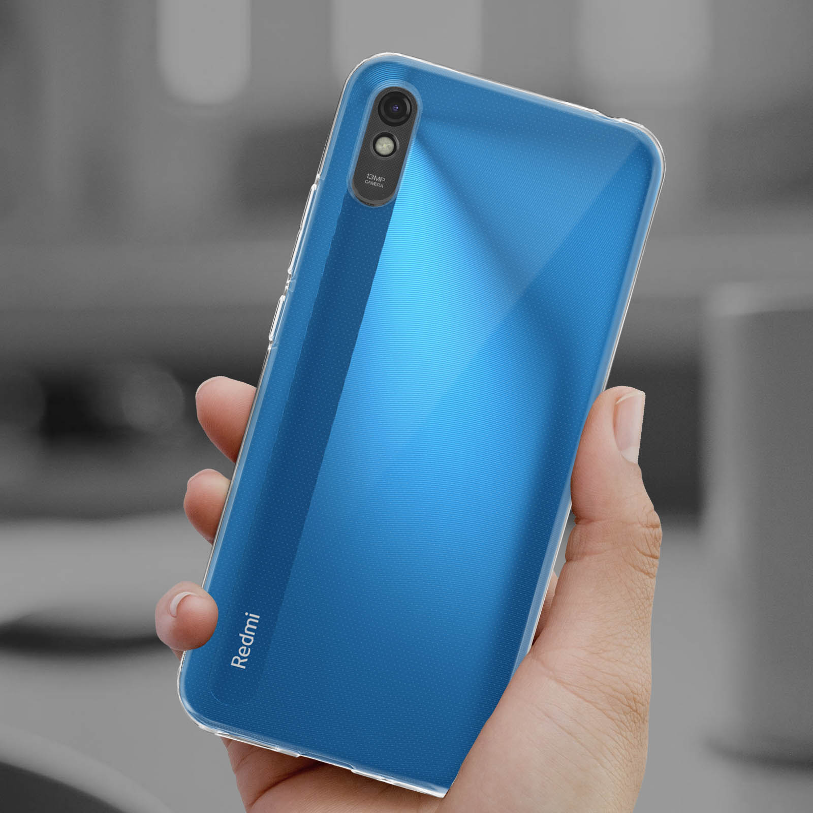 Mano che tiene una custodia trasparente blu per telefono. Logo Redmi visibile. Sfondo sfocato.