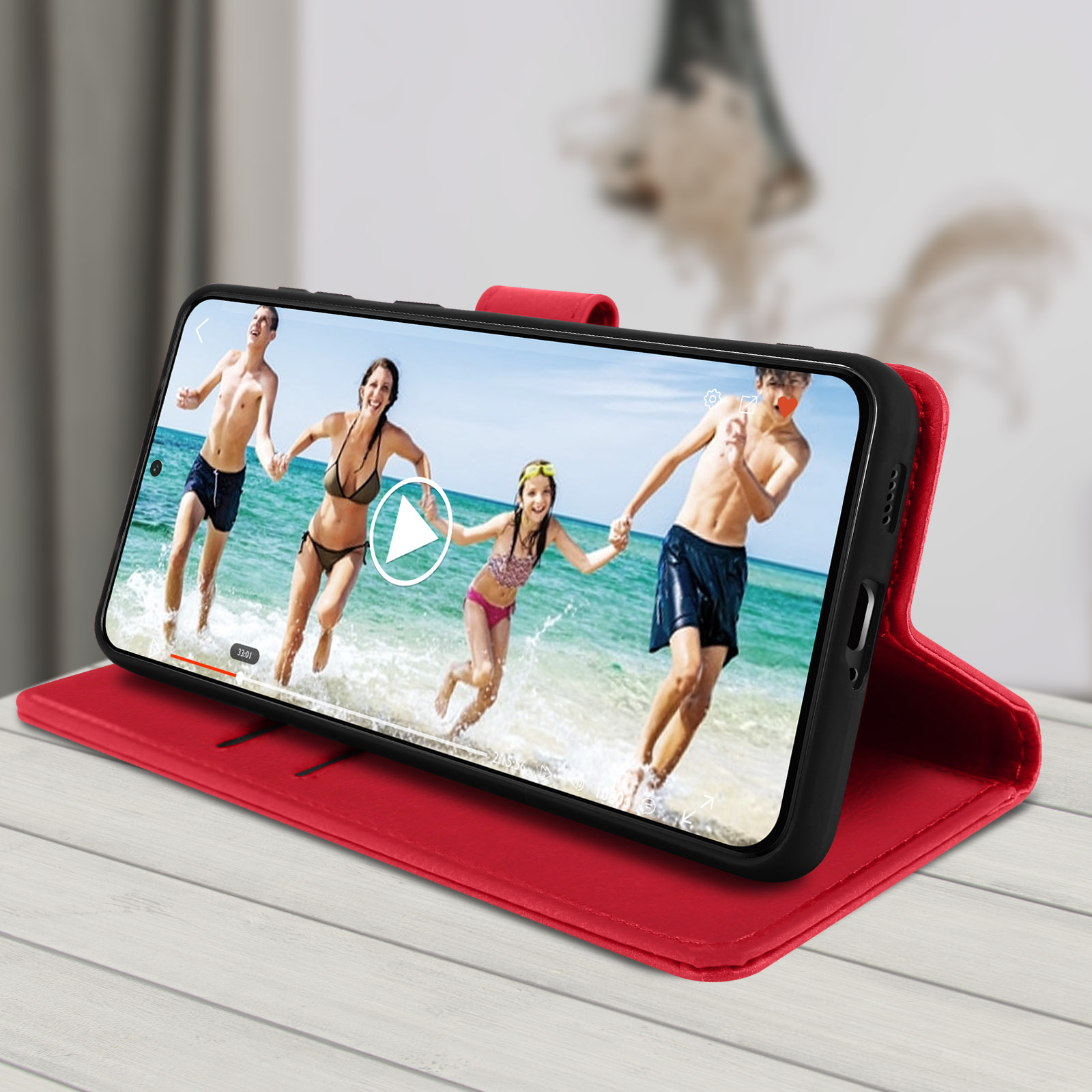 Telefono mostra video di persone in spiaggia. In custodia rossa su tavolo in legno.