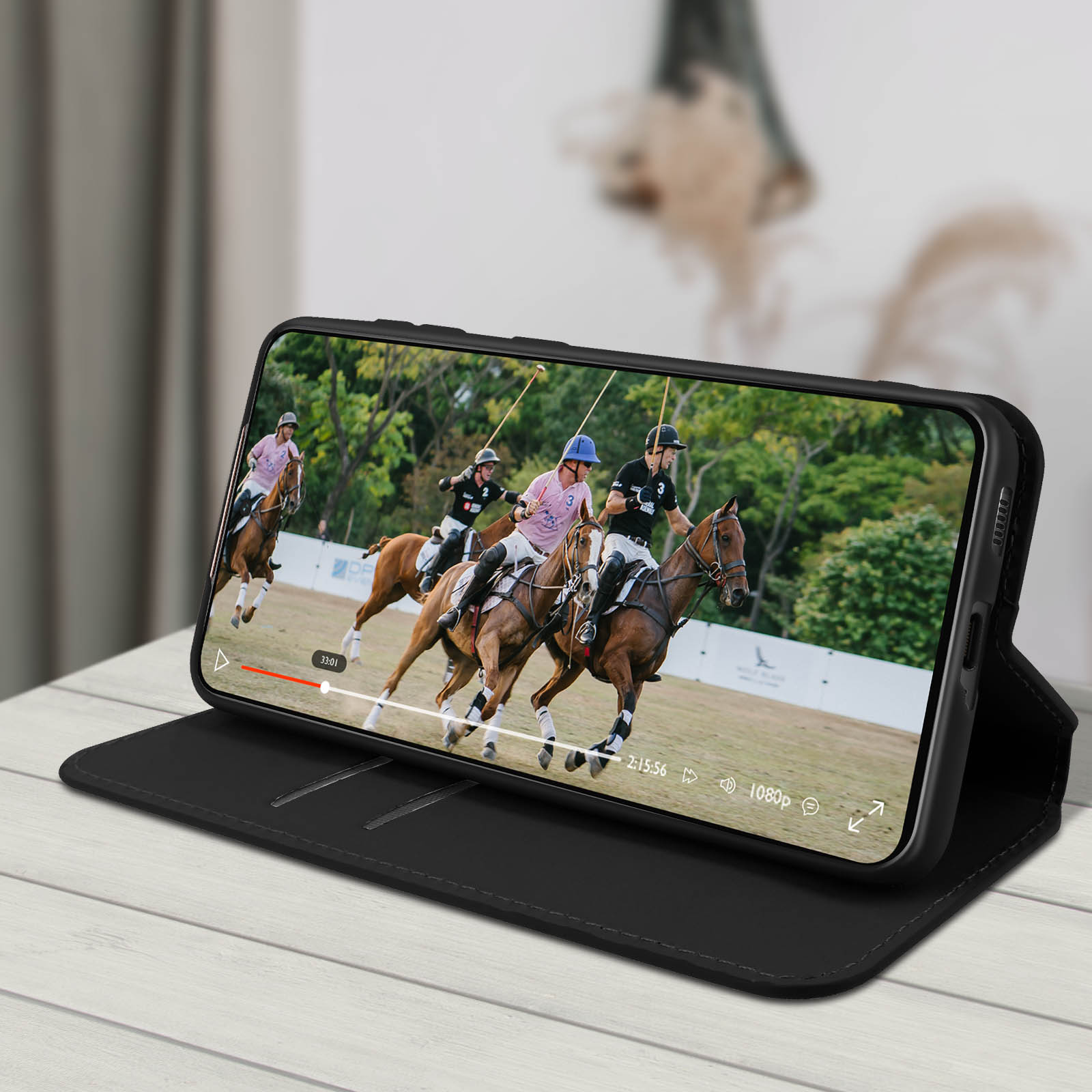 Telefoon met polovideo, opengeklapt op een hoes. Achtergrond: een tafel, wazige details.