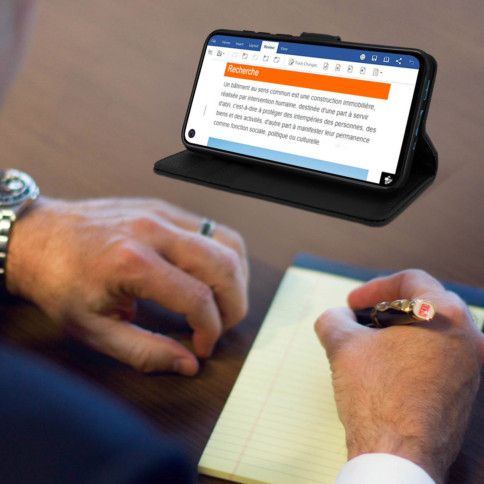 Persona scrive con penna. Telefono mostra documento. Blocco note giallo.