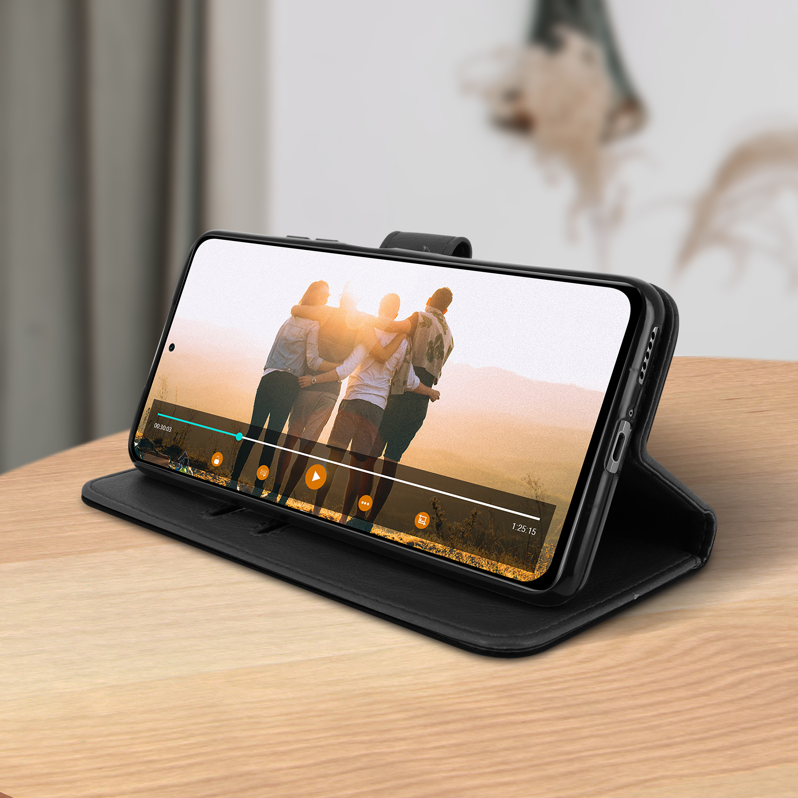 Téléphone dans un étui noir, montrant une vidéo d'amis. Repose sur une table en bois.