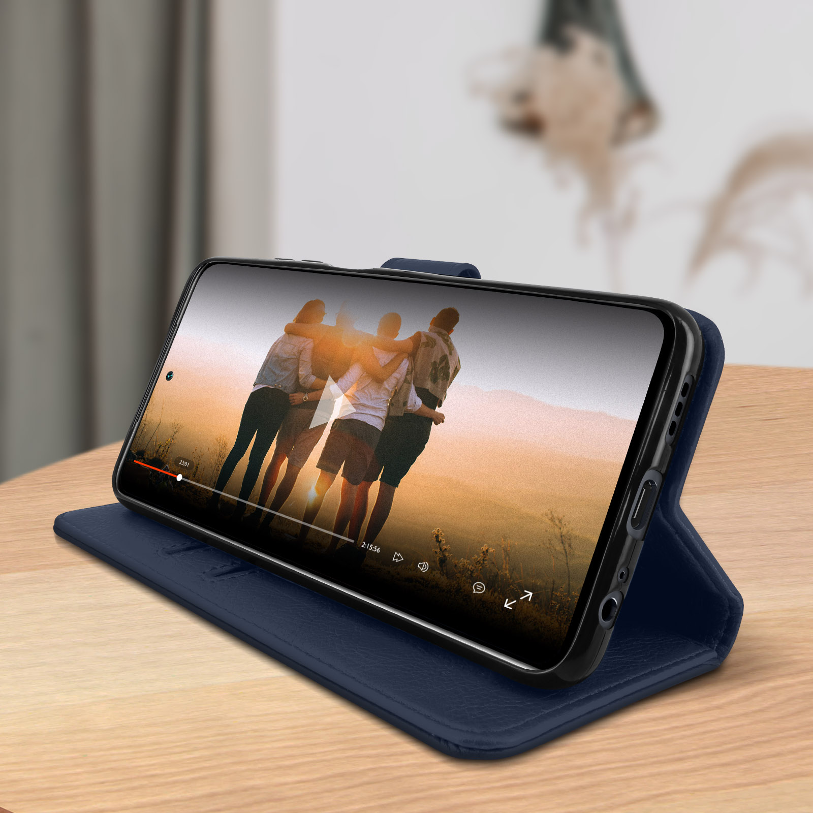 Custodia blu con telefono che mostra un video di amici. Custodia aperta su un tavolo di legno. Sfondo sfocato.