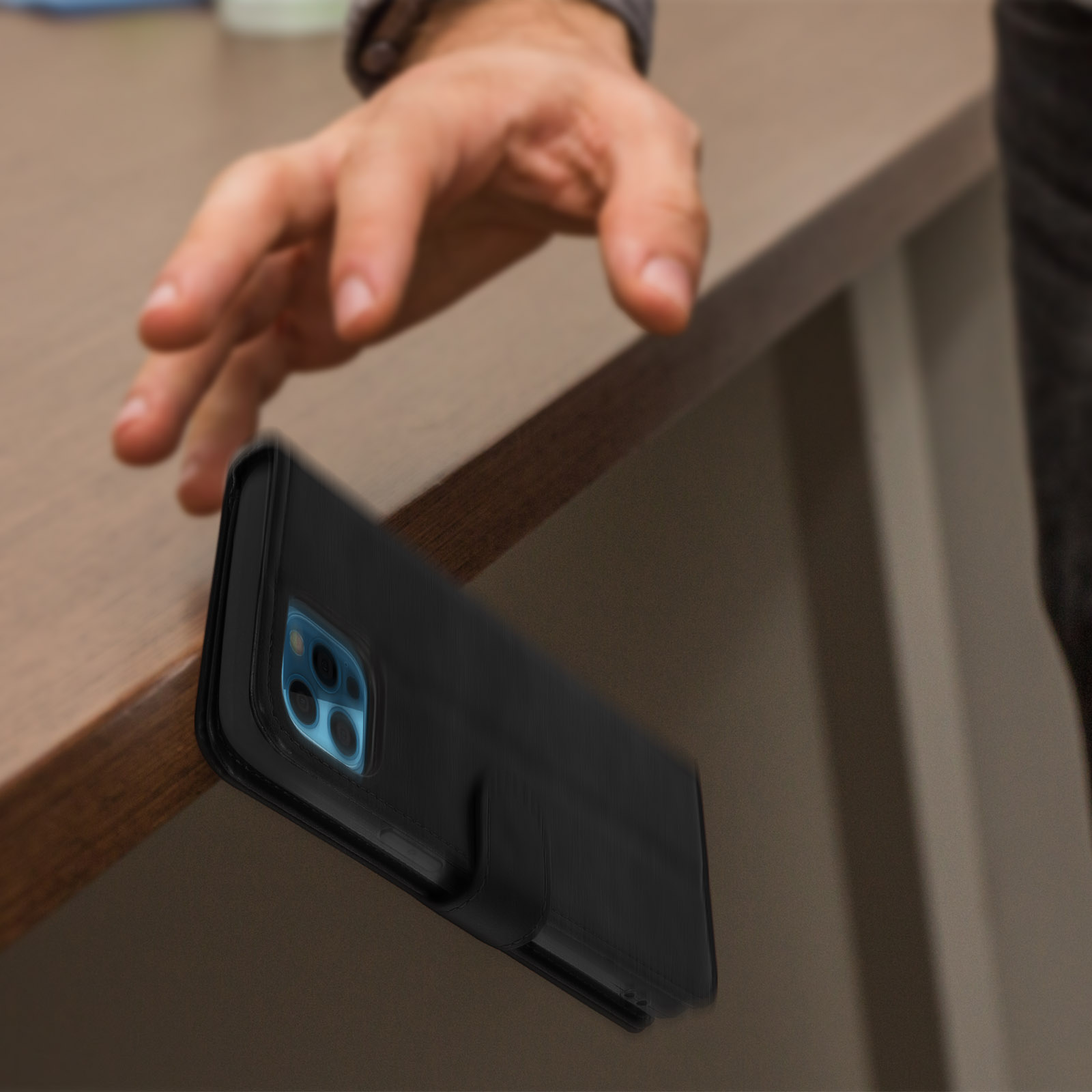 Main tendue vers une coque de téléphone noire au bord d'une surface en bois.