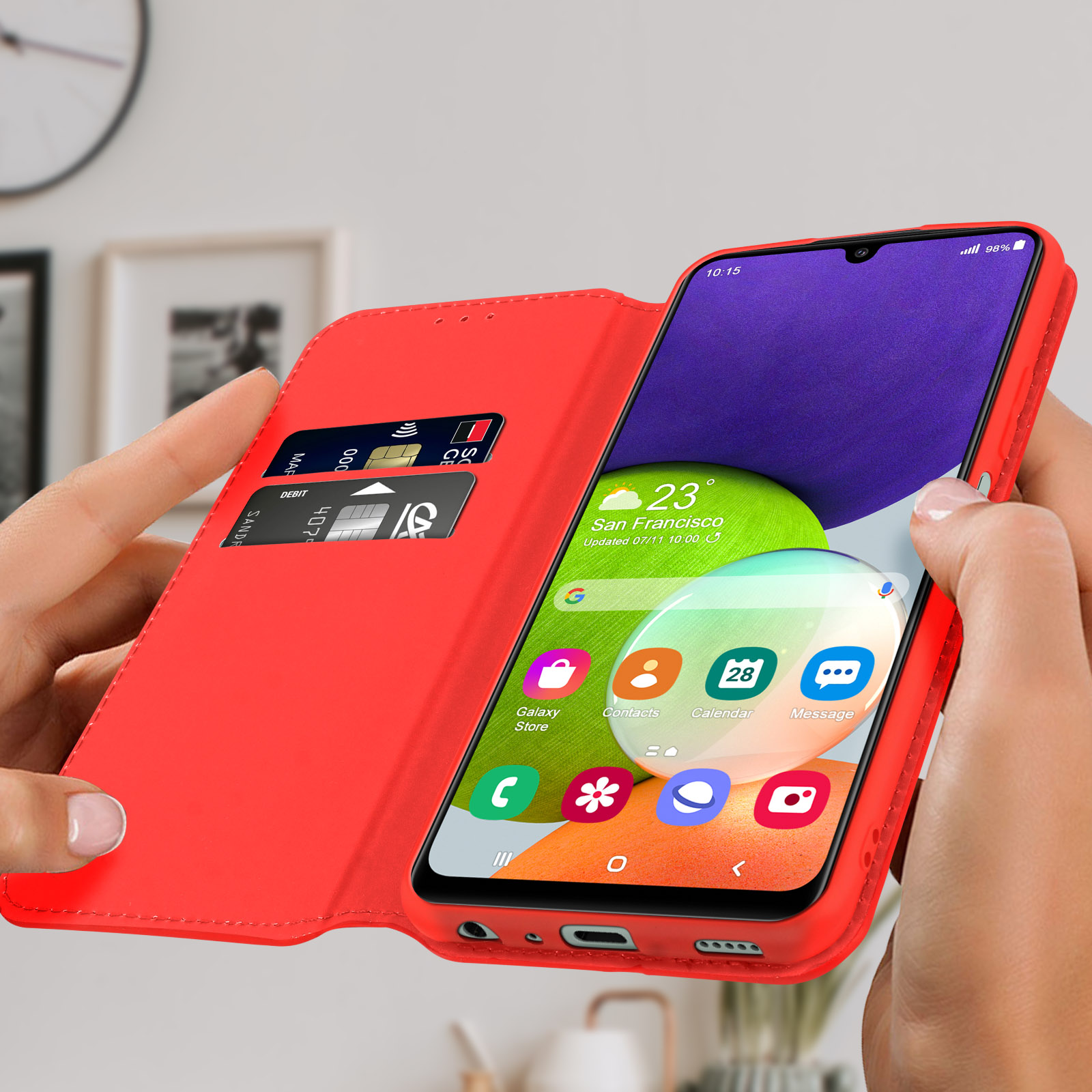 Funda roja, abierta, teléfono mostrando pantalla de inicio. Fondo: objetos borrosos.