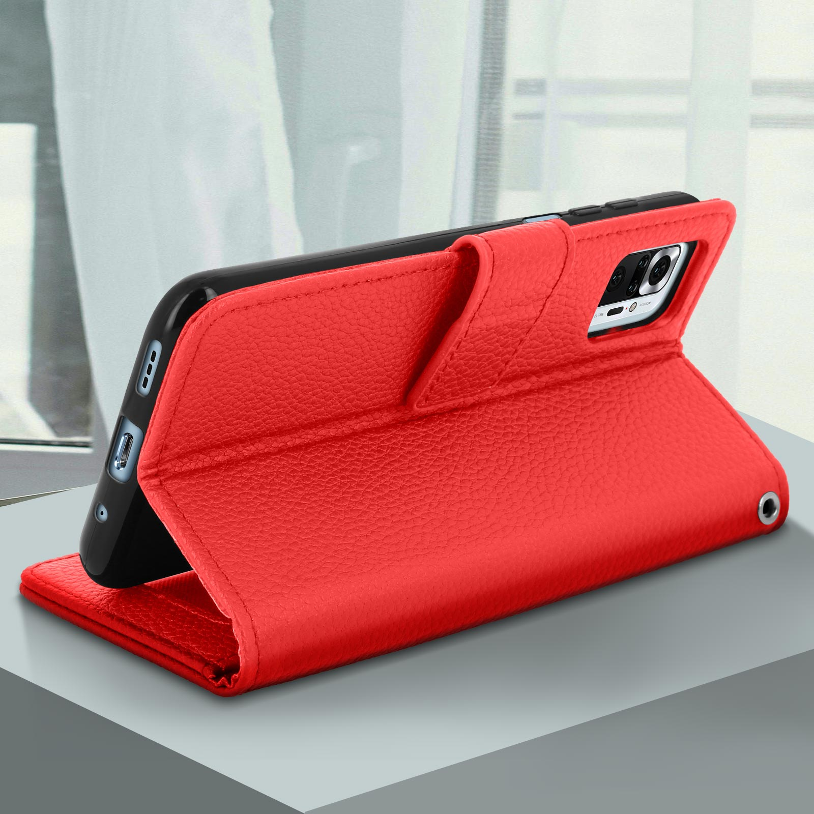 Custodia per telefono in pelle rossa aperta. Telefono all'interno, su una superficie grigia. Finestra visibile.