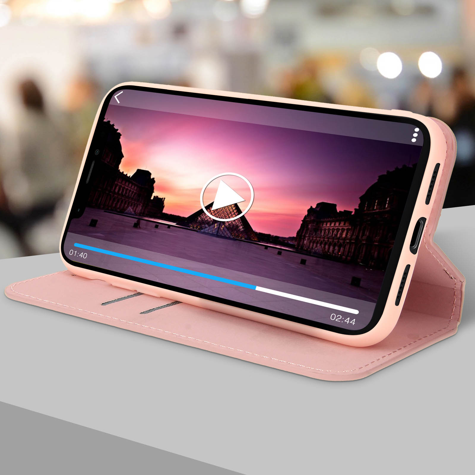 Telefono in custodia rosa che riproduce video di una città, su un tavolo, sfondo sfocato.
