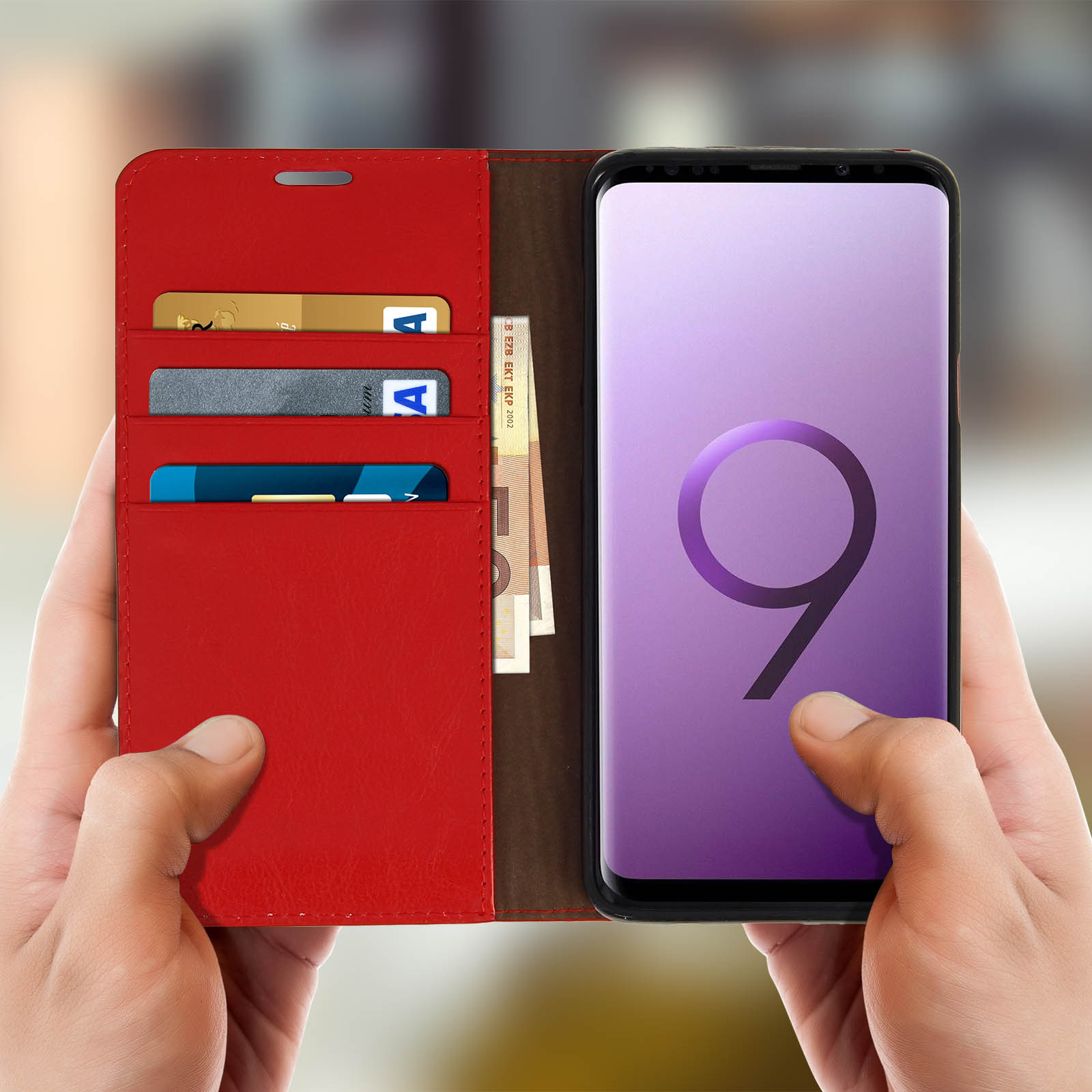 Mano che tiene custodia rossa con carte di credito e contanti, telefono a destra.
