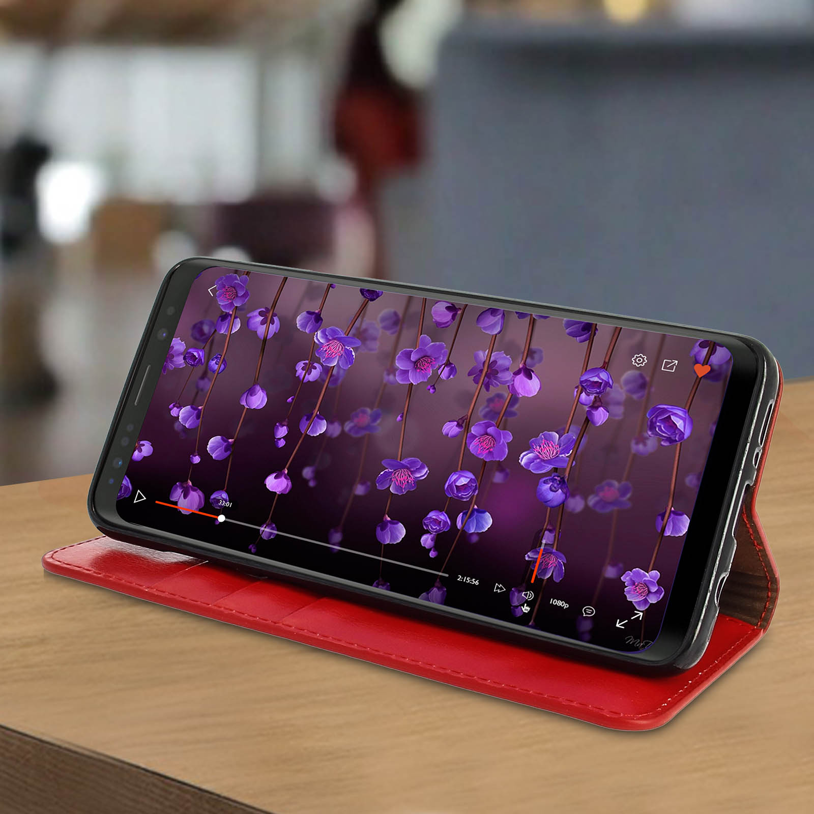 Un telefono che mostra un video floreale su una custodia in pelle rossa su uno sfondo sfocato.