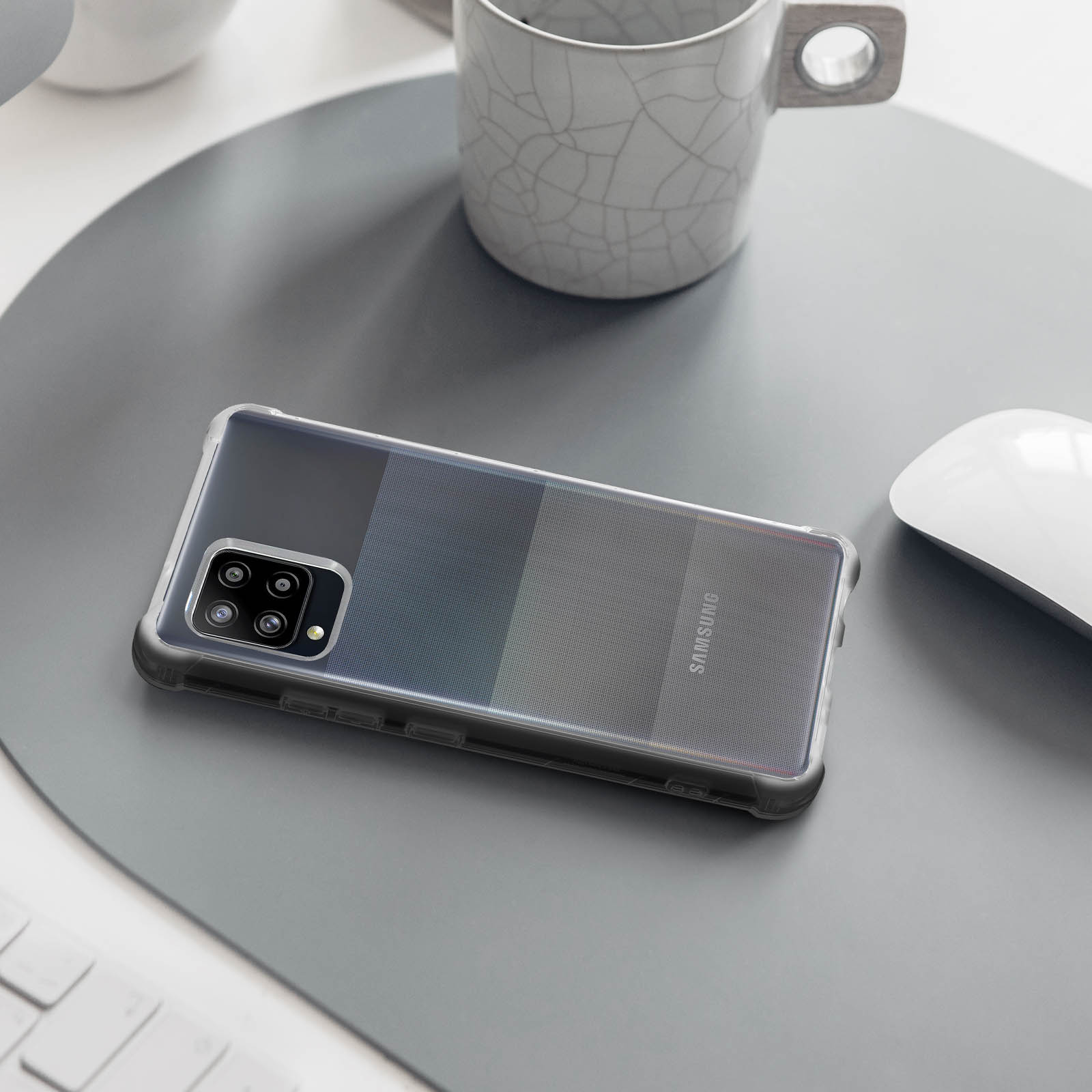 Un telefono in una custodia è appoggiato su un tappetino grigio per scrivania accanto a una tazza e un mouse.