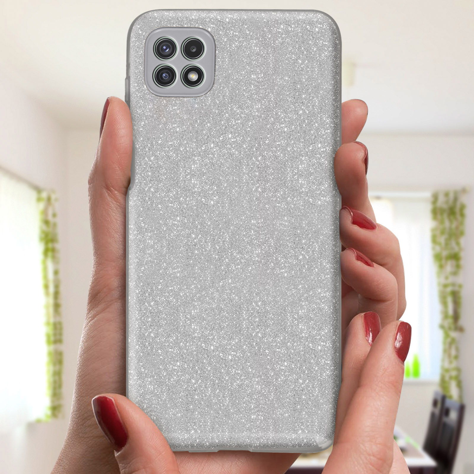 Una donna tiene una custodia per telefono glitterata argentata. La custodia è su un telefono, con una fotocamera sul retro.