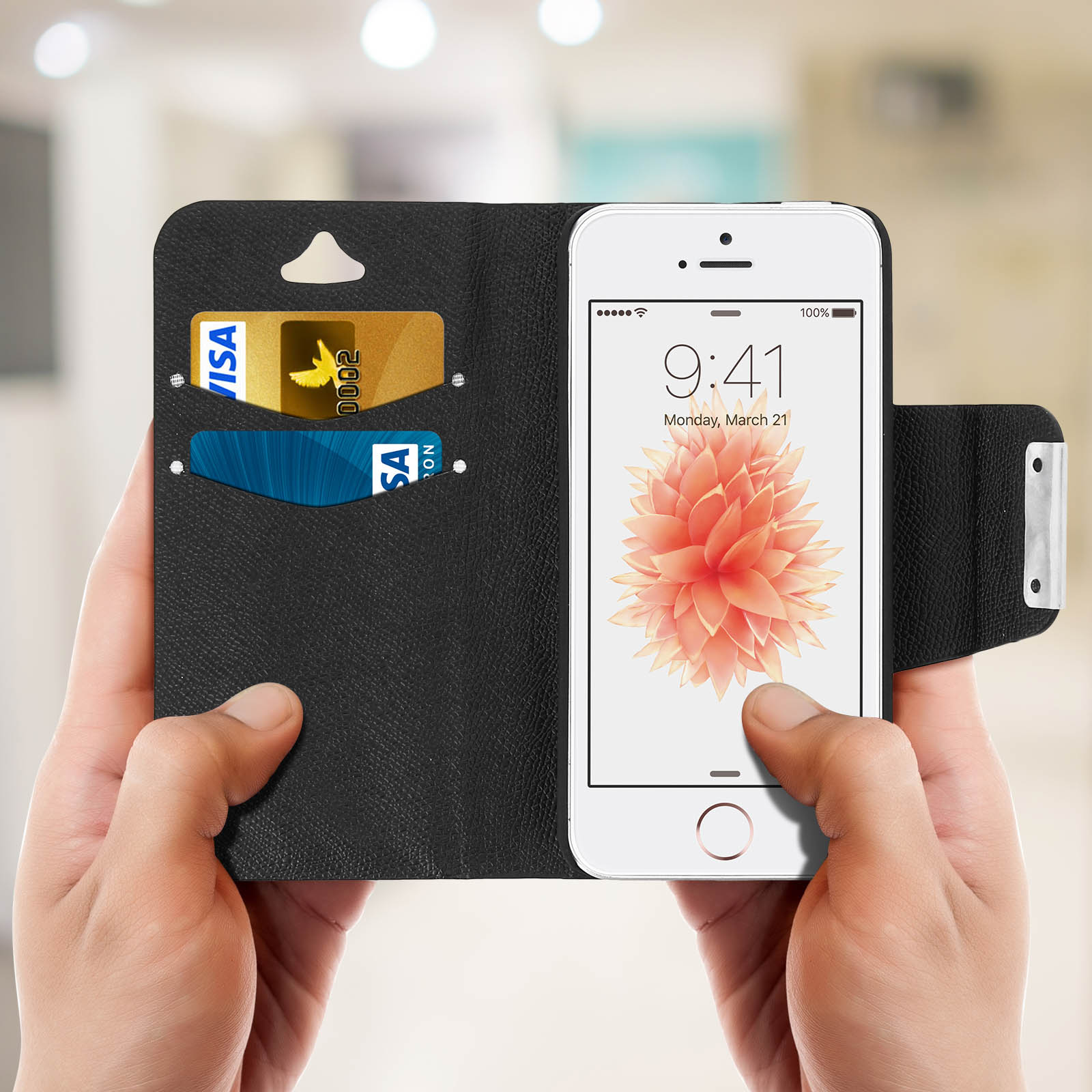 Telefono in una custodia nera con carte di credito all'interno, tenuto da due mani, con carta da parati floreale.