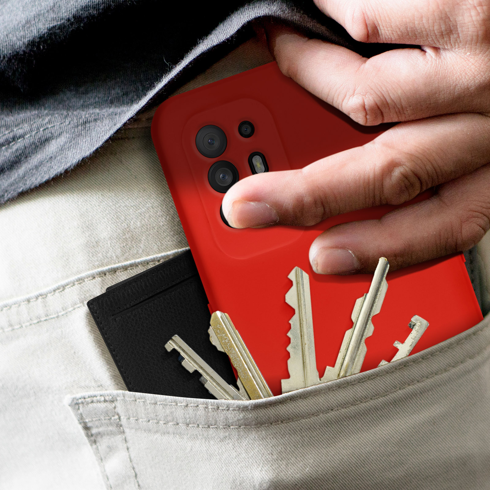 Main d'une personne dans une poche tenant une coque rouge, des clés et un portefeuille noir.