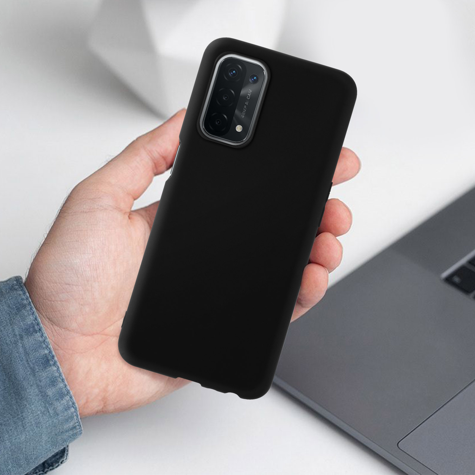 Une main tenant un téléphone noir. Le téléphone a un dos noir et est posé sur une table.