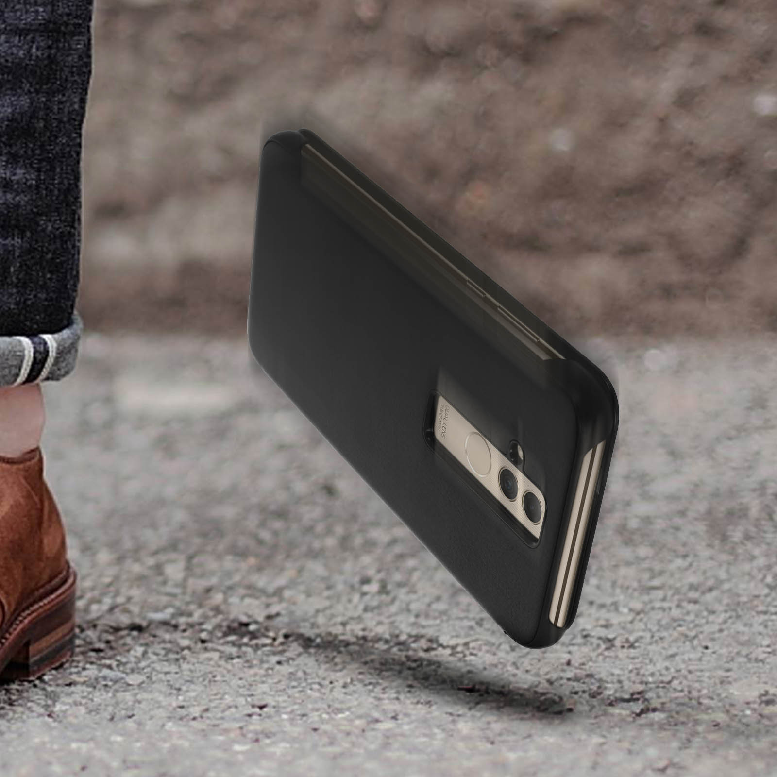 Custodia nera per telefono che cade su una superficie ruvida. Una persona indossa jeans e scarpe marroni.