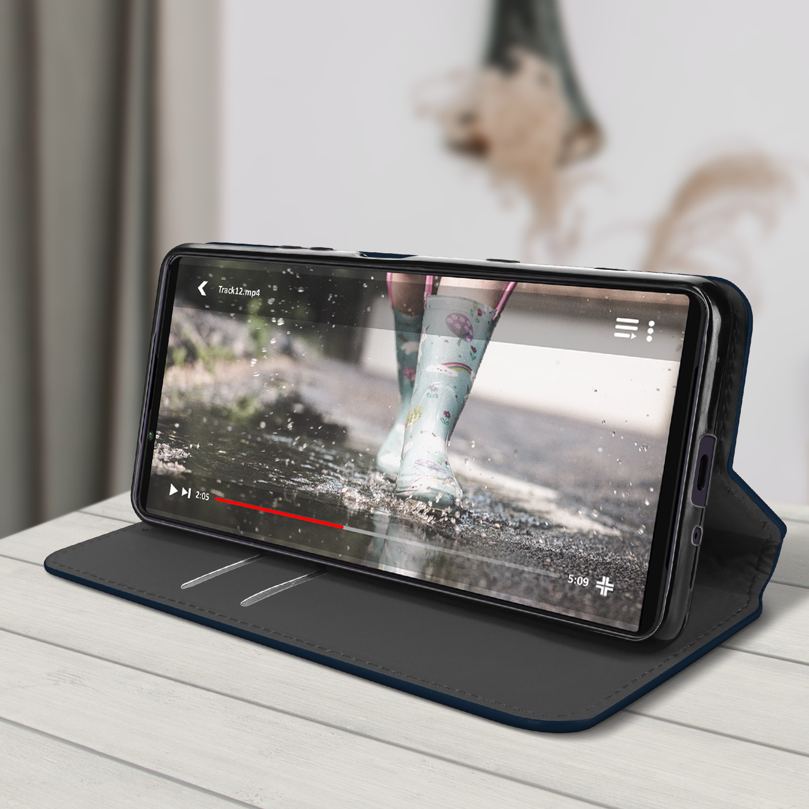 Il telefono mostra video di stivali in pozzanghera. Custodia blu scuro su legno.