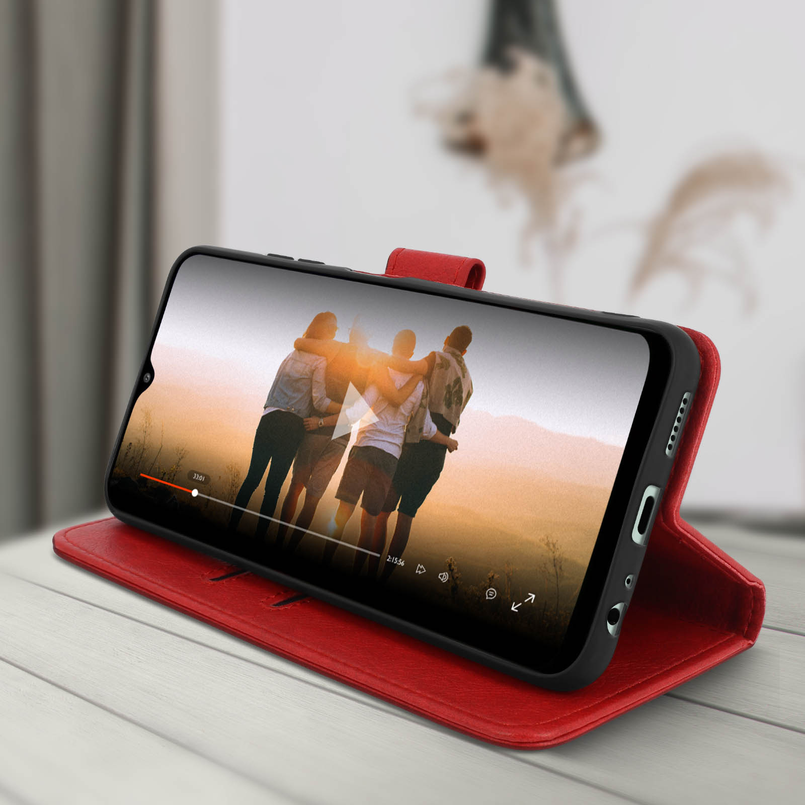 Telefoon in rode portemonneehoes toont video van mensen. De hoes is open. Houten bureau.